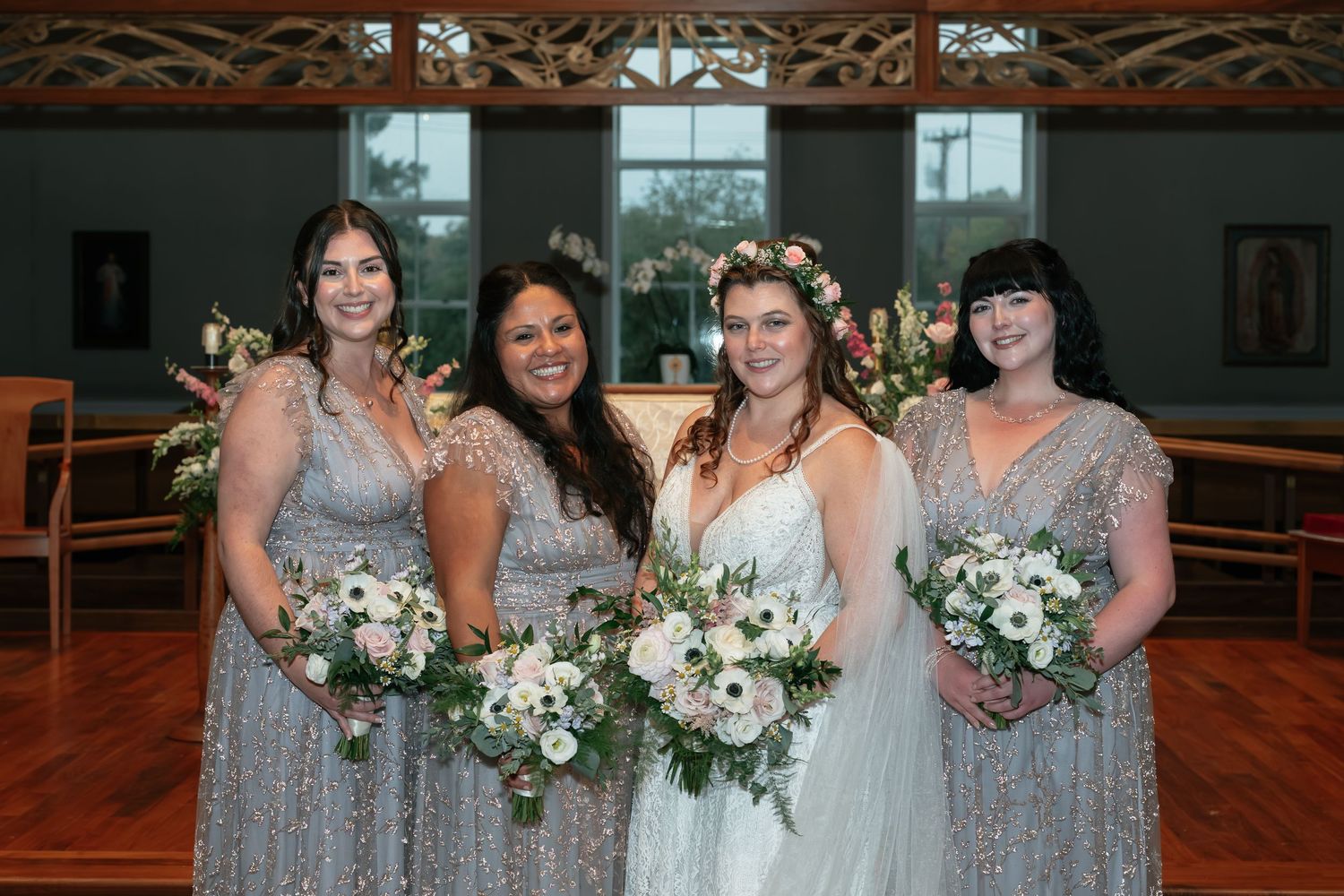 Bridal party in silver sequined dresses holds white and green bouquets in church setting.