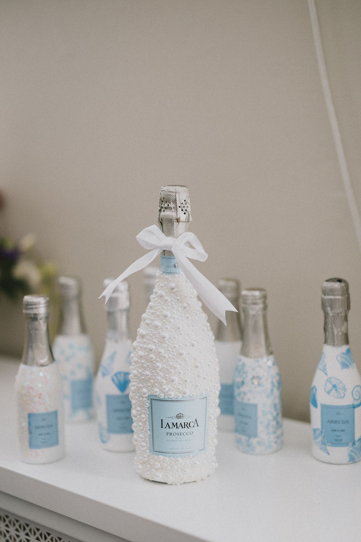 Decorated miniature bottles with white lace and blue ribbons arranged in a row.