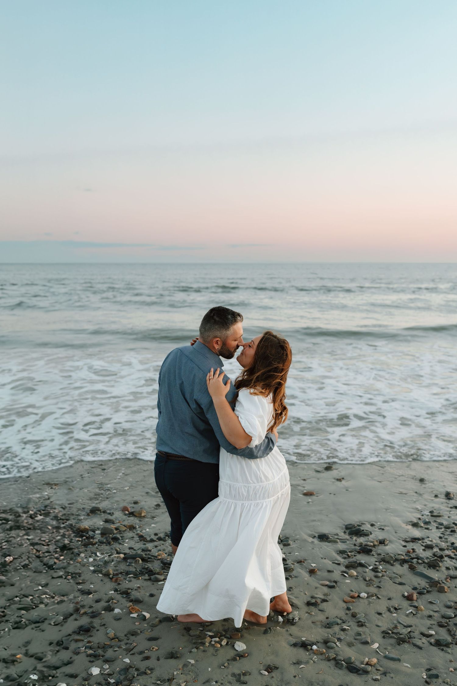 Couple shares tender moments on a misty beach during golden hour.
