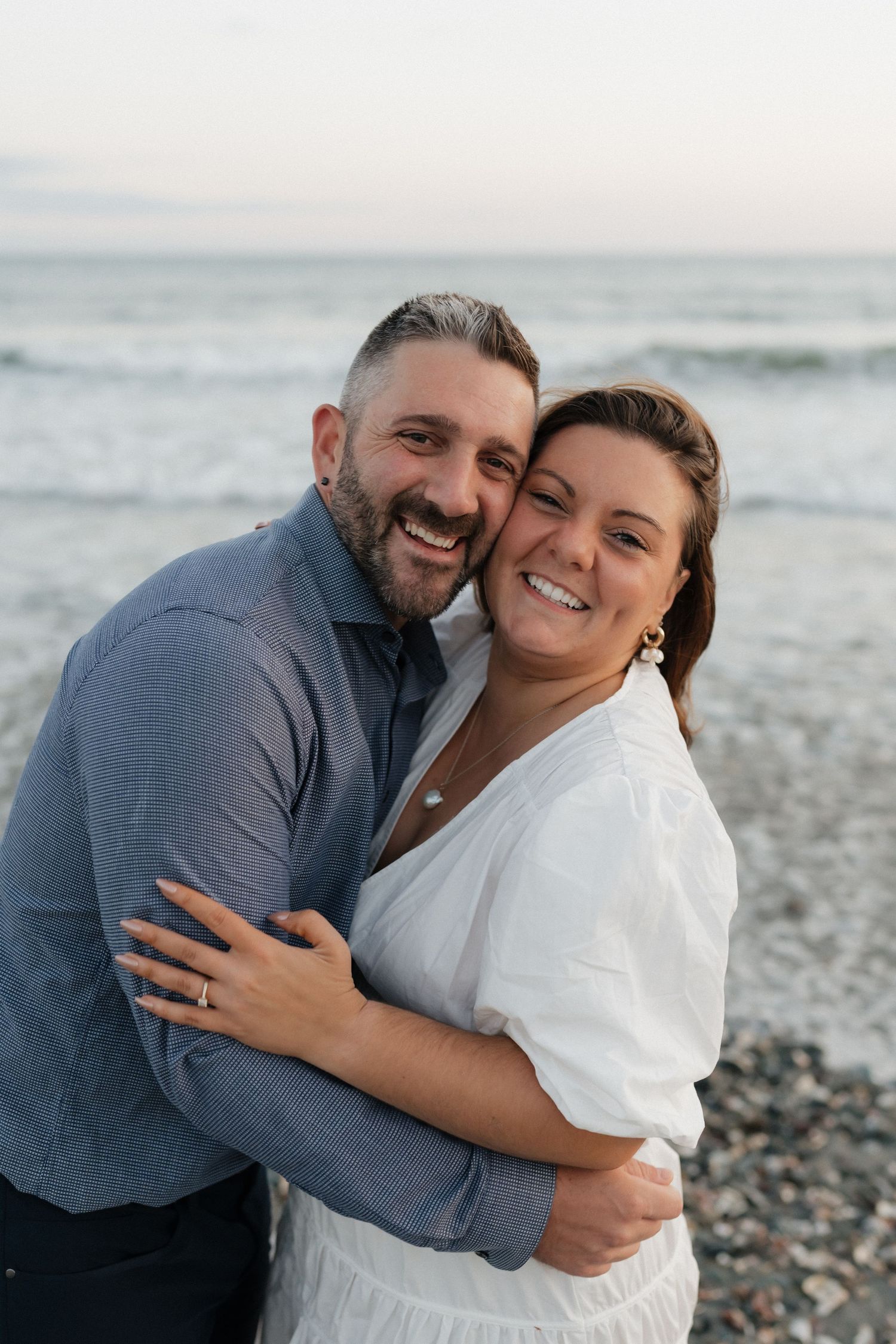 A happy couple embraces on the beach with ocean waves in the background.
