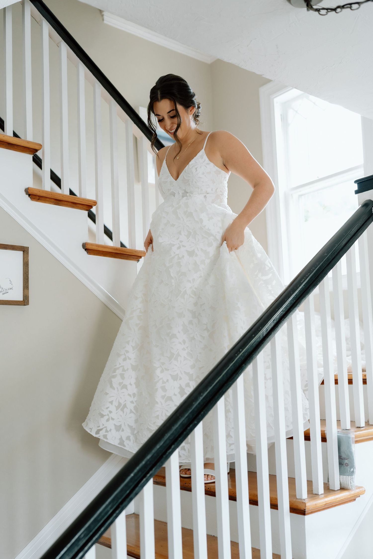 Bride in lace wedding gown standing on wooden staircase with white railings.