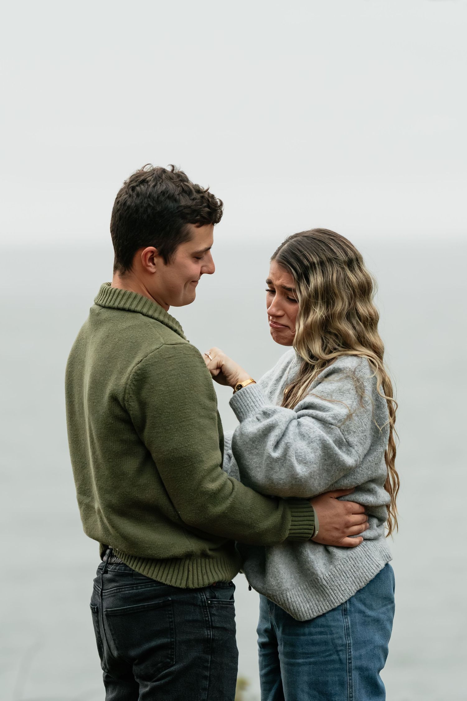 A couple shares an intimate moment wearing cozy sweaters by the ocean.