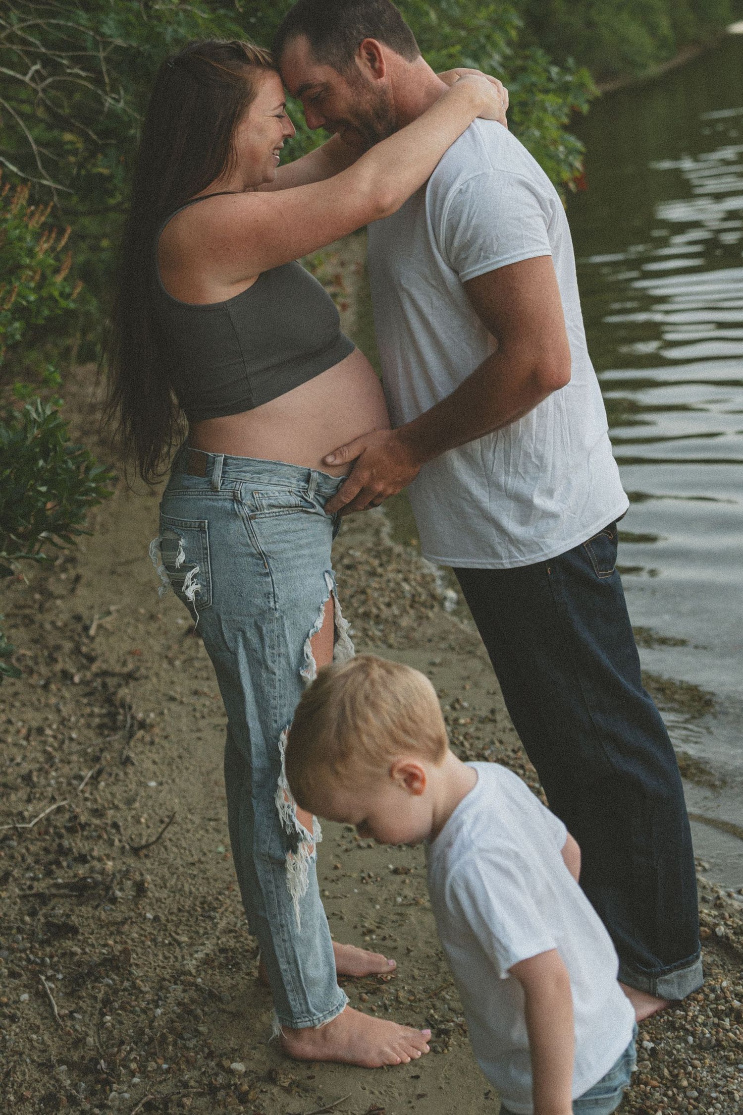 A tender family moment is captured along a tree-lined riverbank.