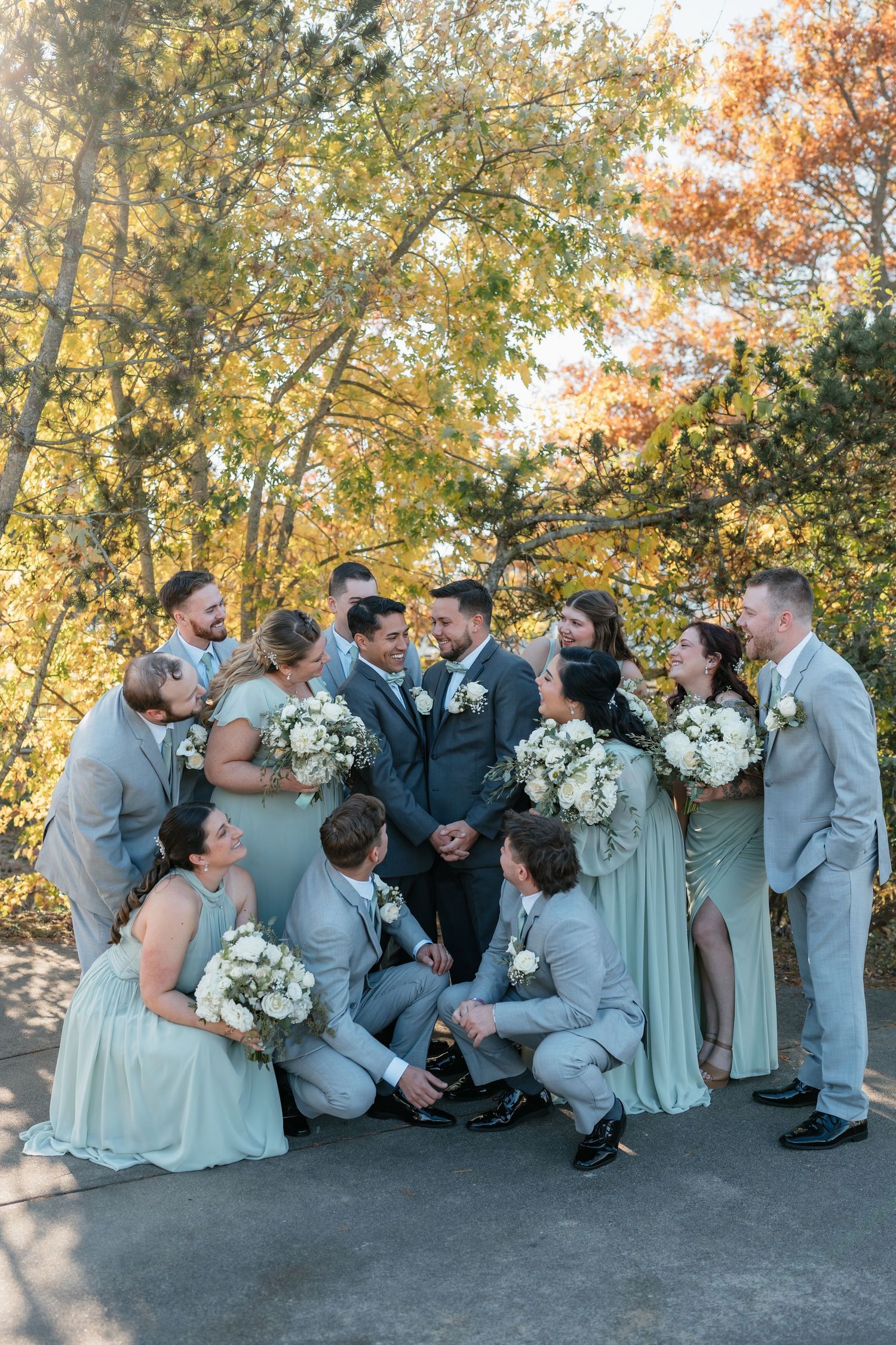 Wedding party in mint green and gray attire poses together outdoors during autumn.