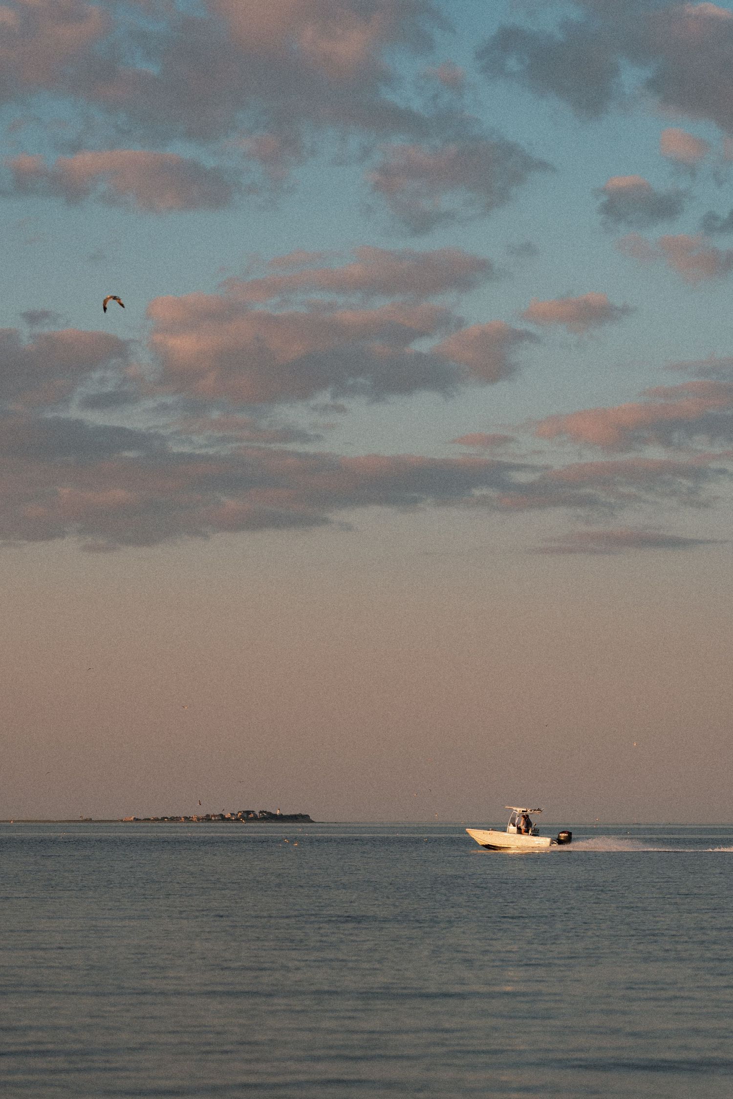 Distant boat cruises across calm ocean waters under pink and blue cloudy sunset sky.