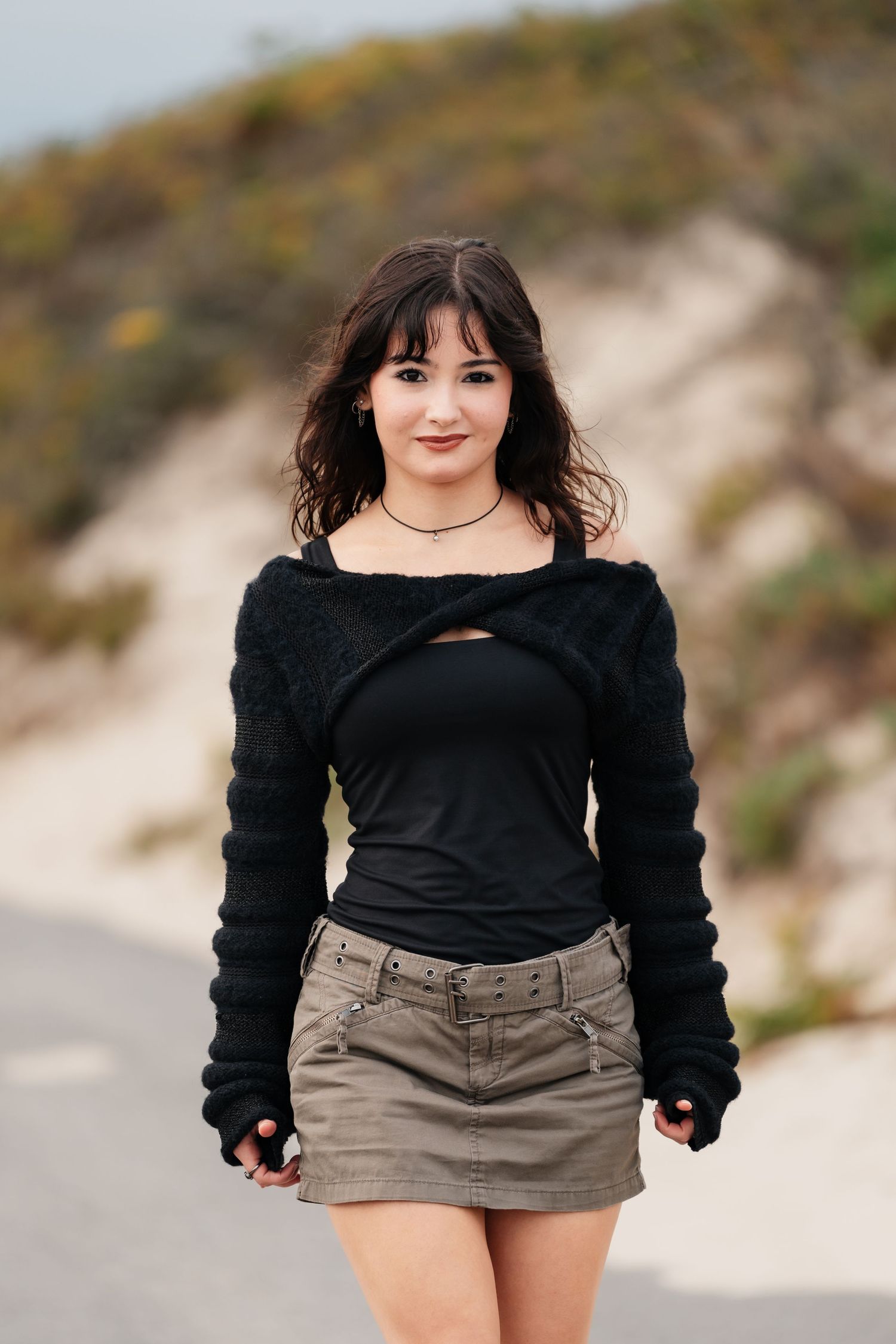 Person wearing black top and khaki shorts poses on beach path.