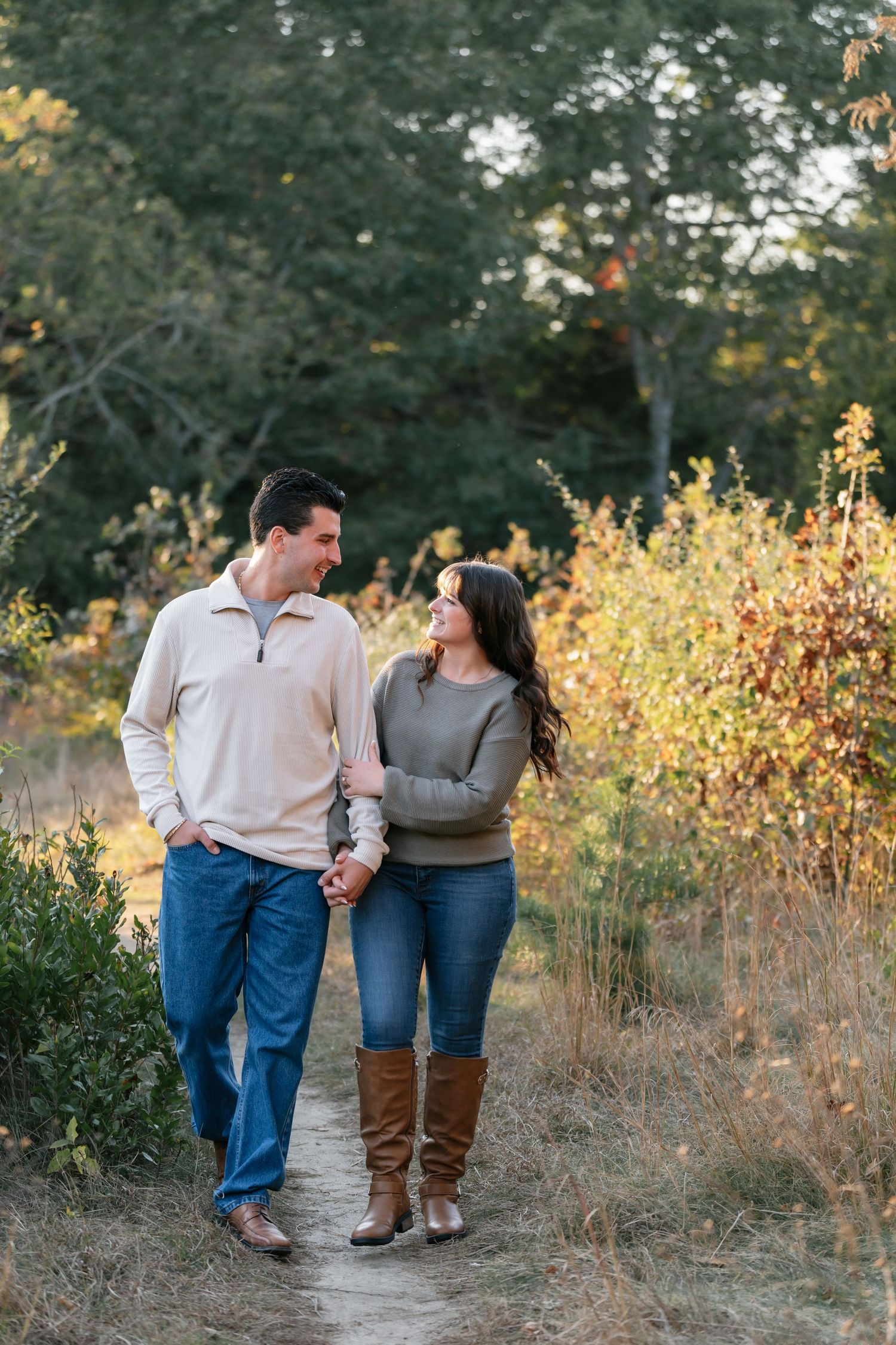 A couple walks hand in hand through a golden autumn field at sunset.