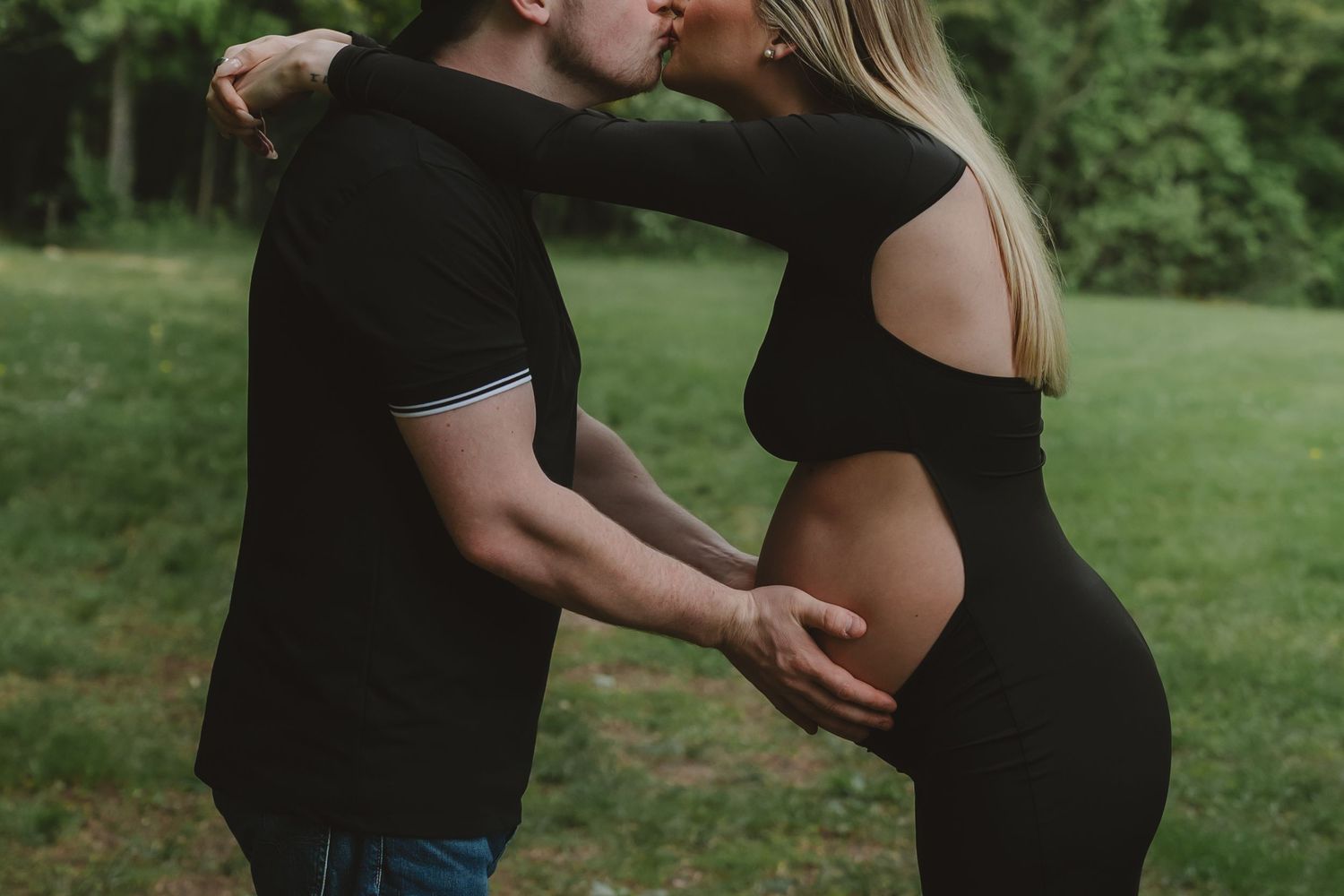 A romantic maternity photoshoot shows a couple embracing in a lush green outdoor setting.