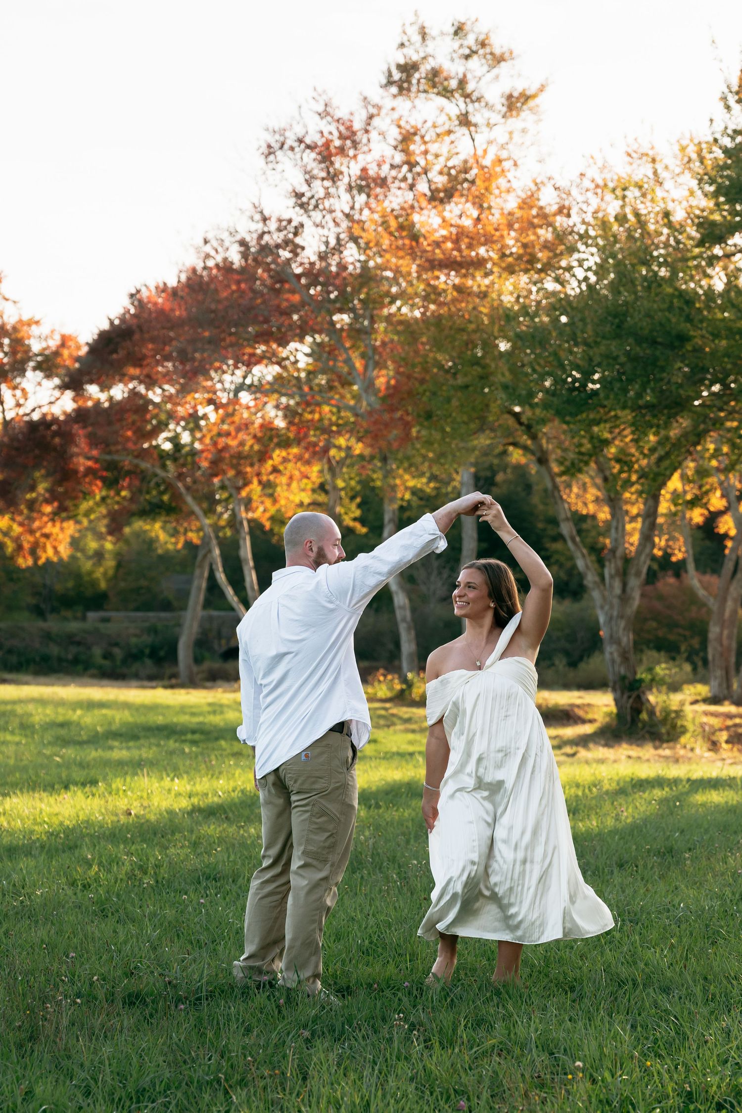 A couple dances joyfully in a meadow during golden hour.