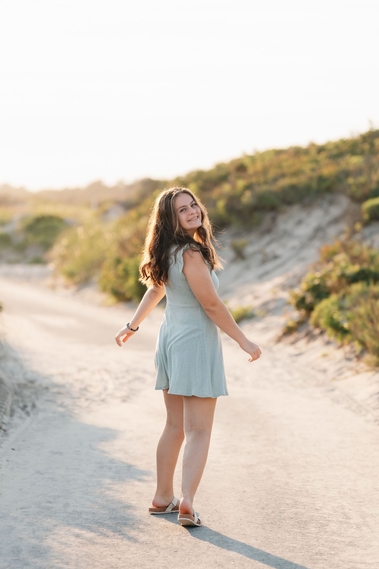Joyful twirl in mint dress on sandy beach path during golden hour.