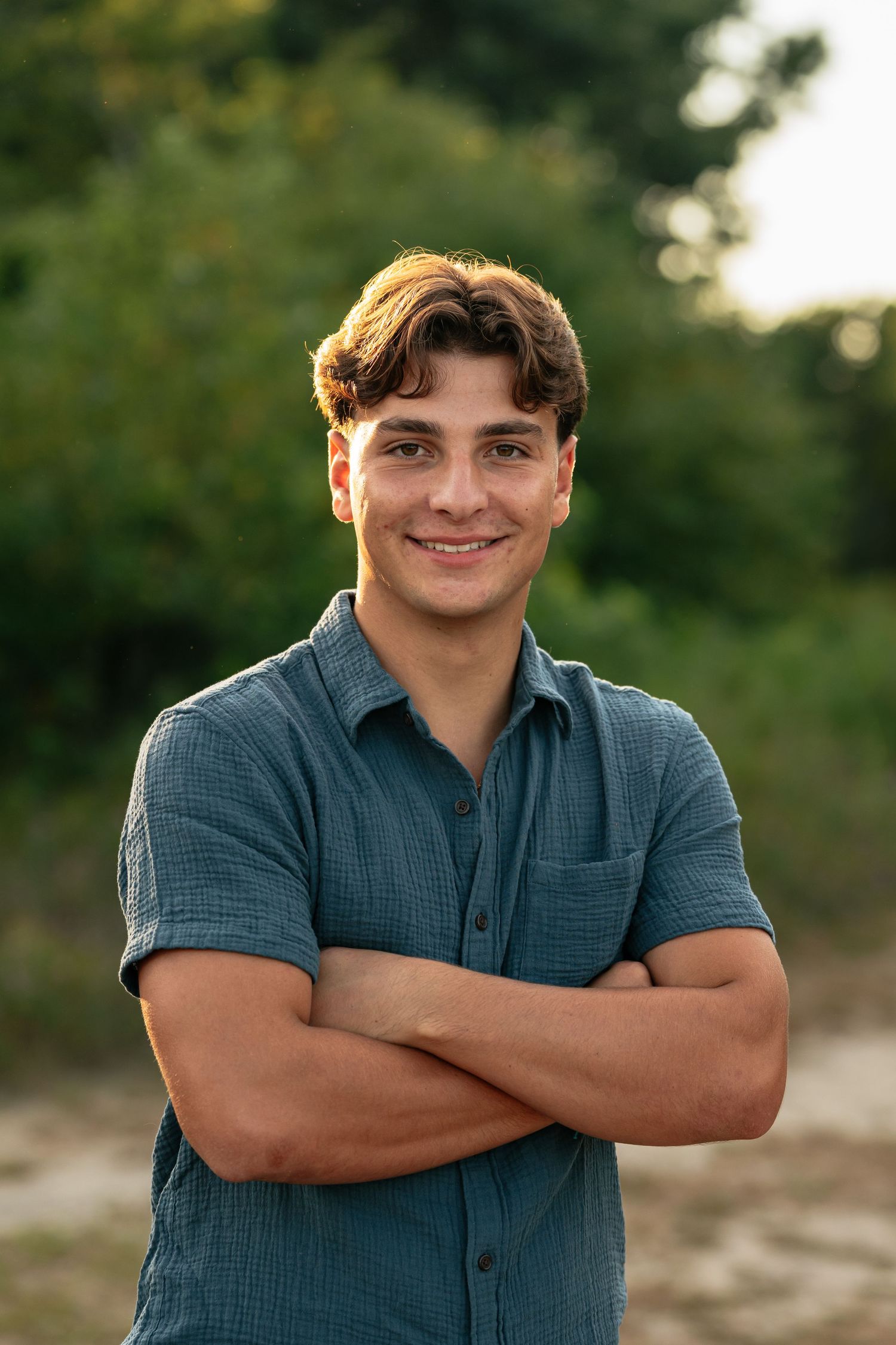 Relaxed pose in navy shirt against natural greenery background.