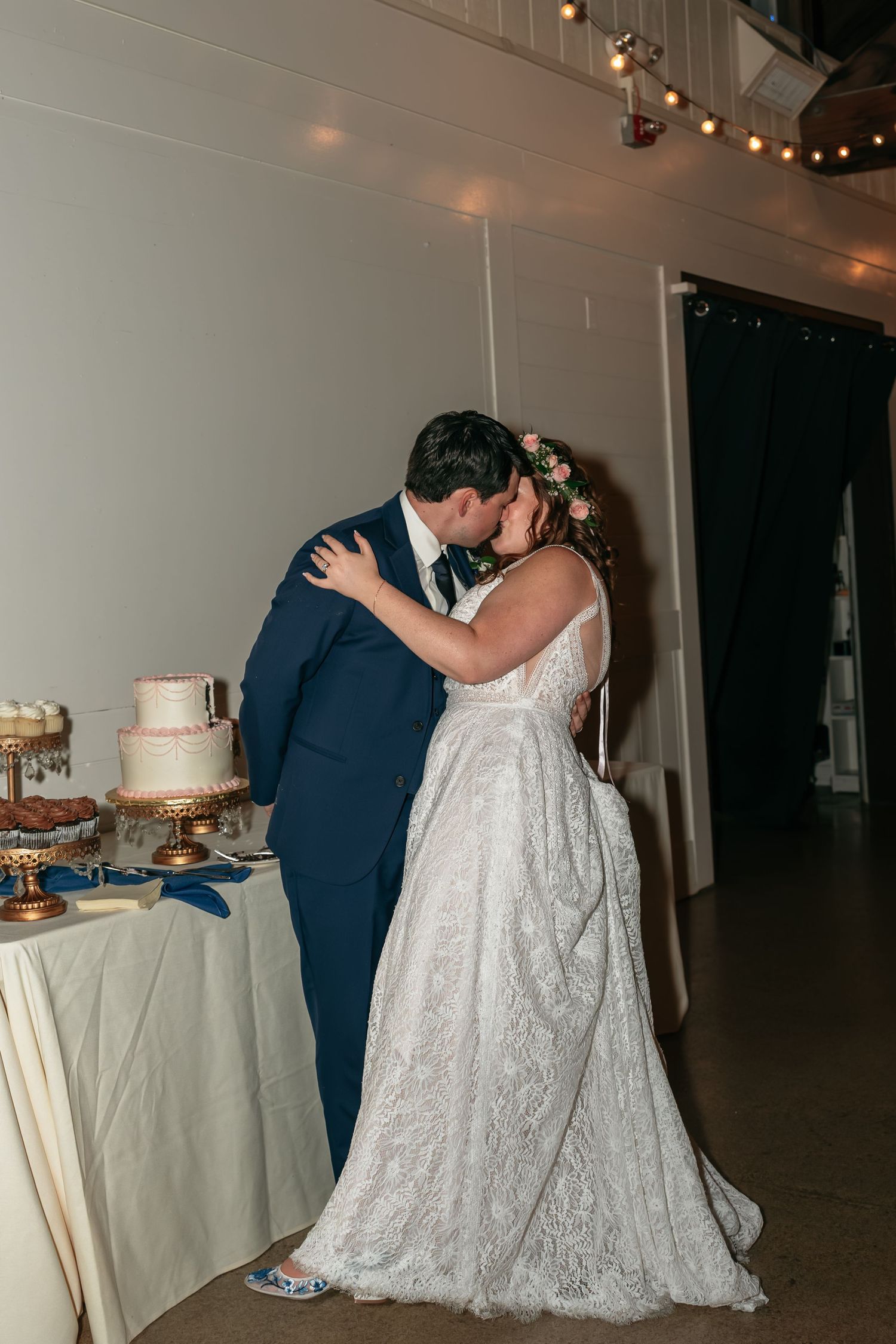 A couple shares their first dance at their wedding reception next to an elegant white wedding cake.