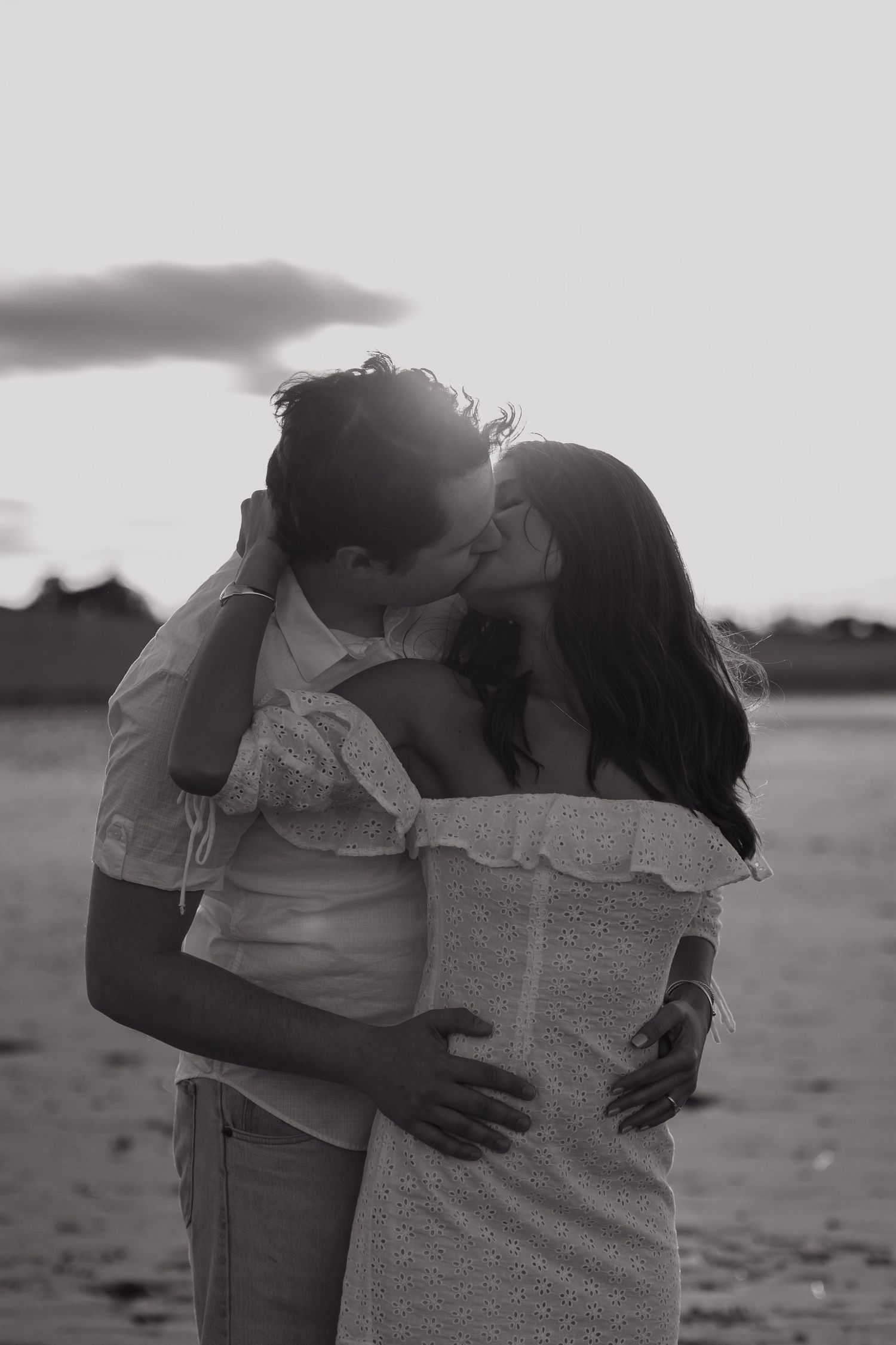 A black and white photo captures an intimate embrace on a misty beach.