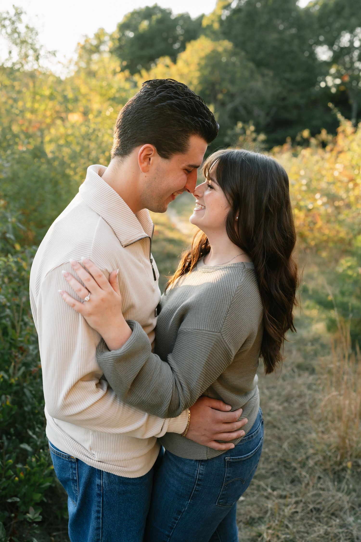 A couple embraces lovingly in a sunlit field with autumn foliage.