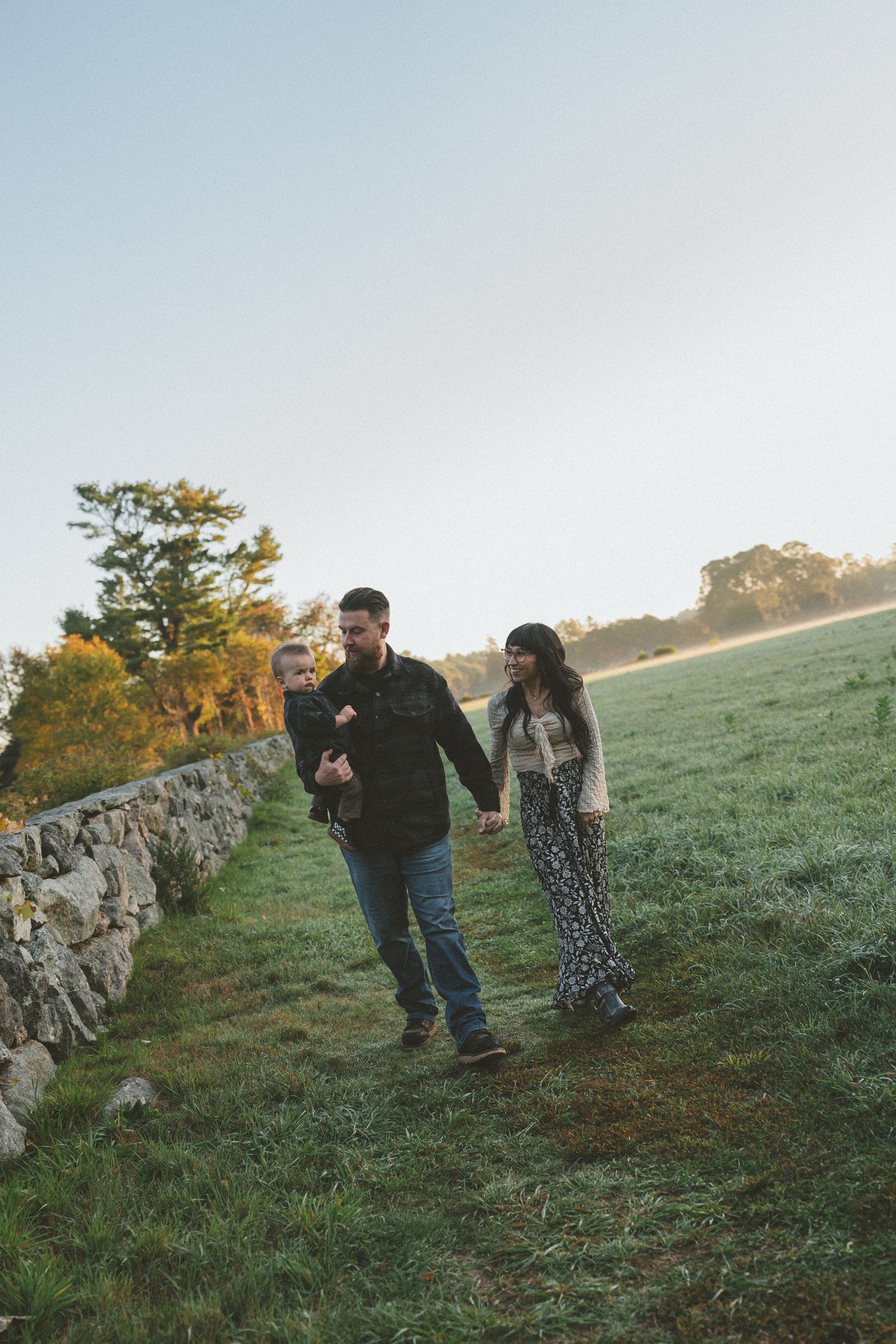 Playful interaction near a rustic stone wall on a grassy hillside at sunset.