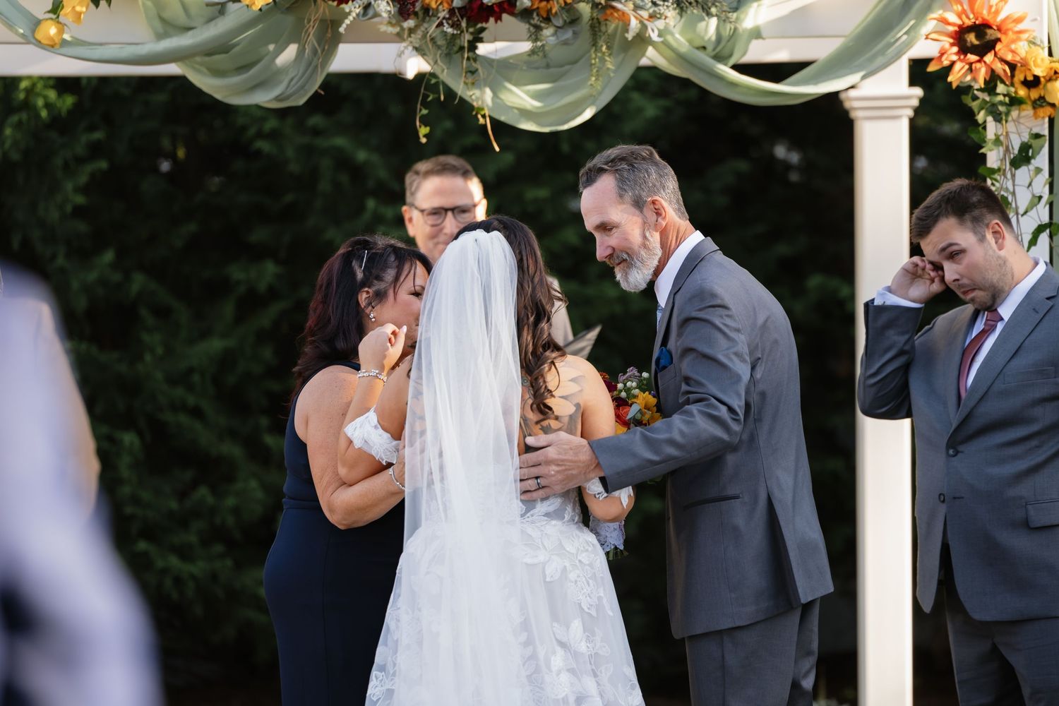 Wedding ceremony under a white arbor decorated with autumn flowers and greenery.