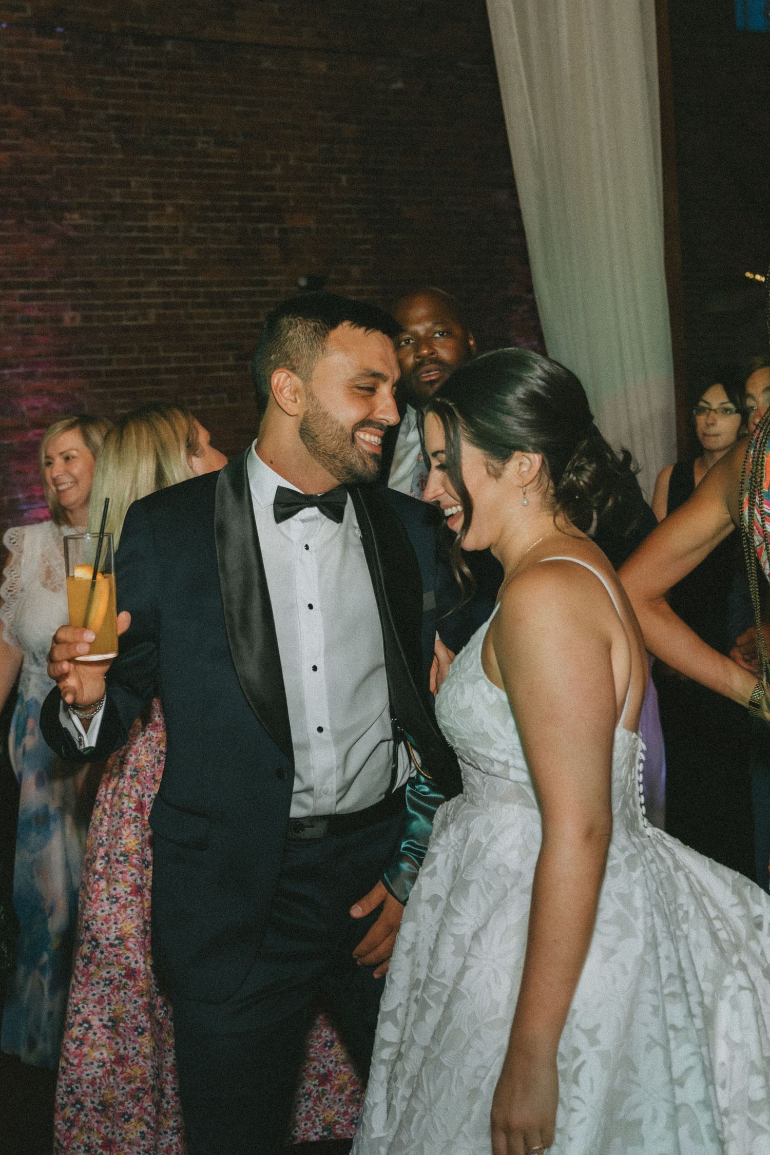 Wedding guests dancing and celebrating together on the dance floor at an indoor reception venue.
