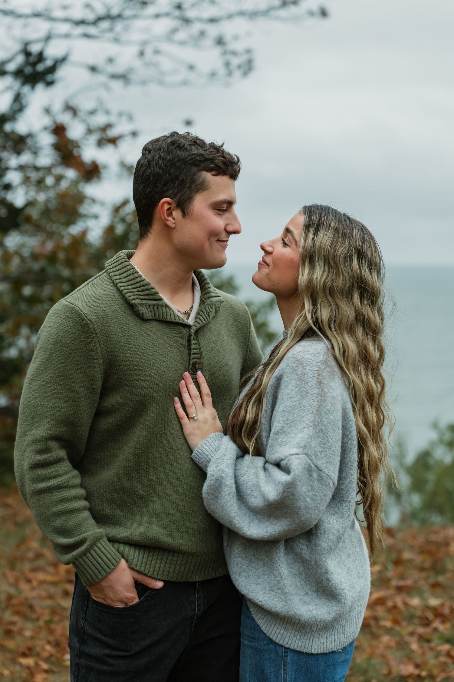 Couple in sweaters sharing intimate moment among fall foliage.