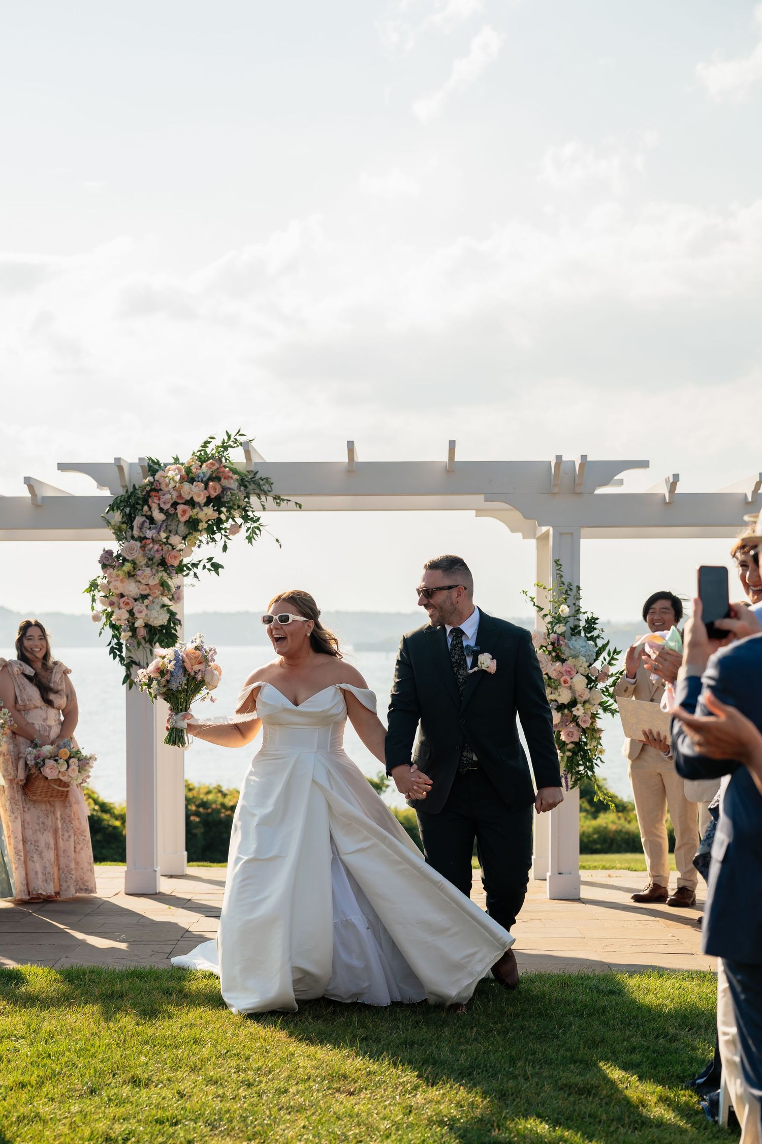 Newlyweds exit ceremony under white pergola decorated with pink floral arrangements.