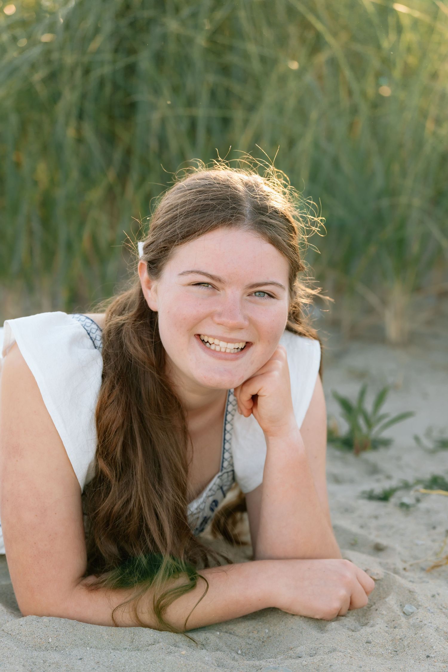 Candid beach photo of someone in white dress lying on sand with natural lighting.
