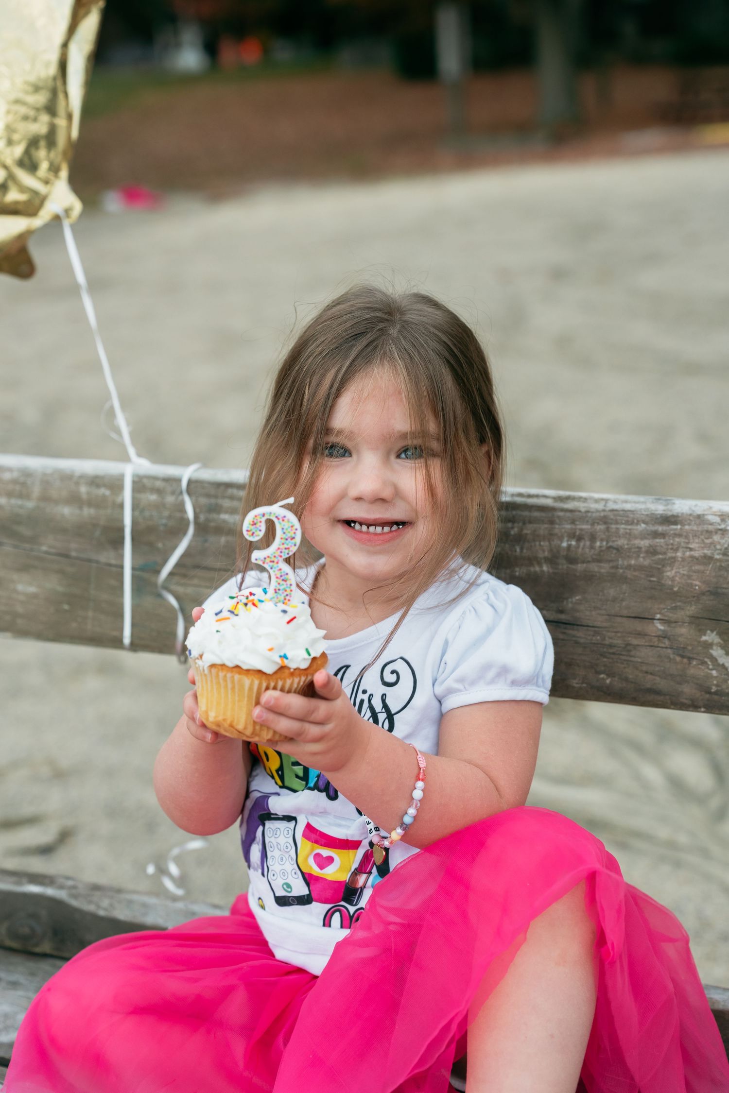 A decorated cupcake is being enjoyed while sitting on a wooden bench at the beach.