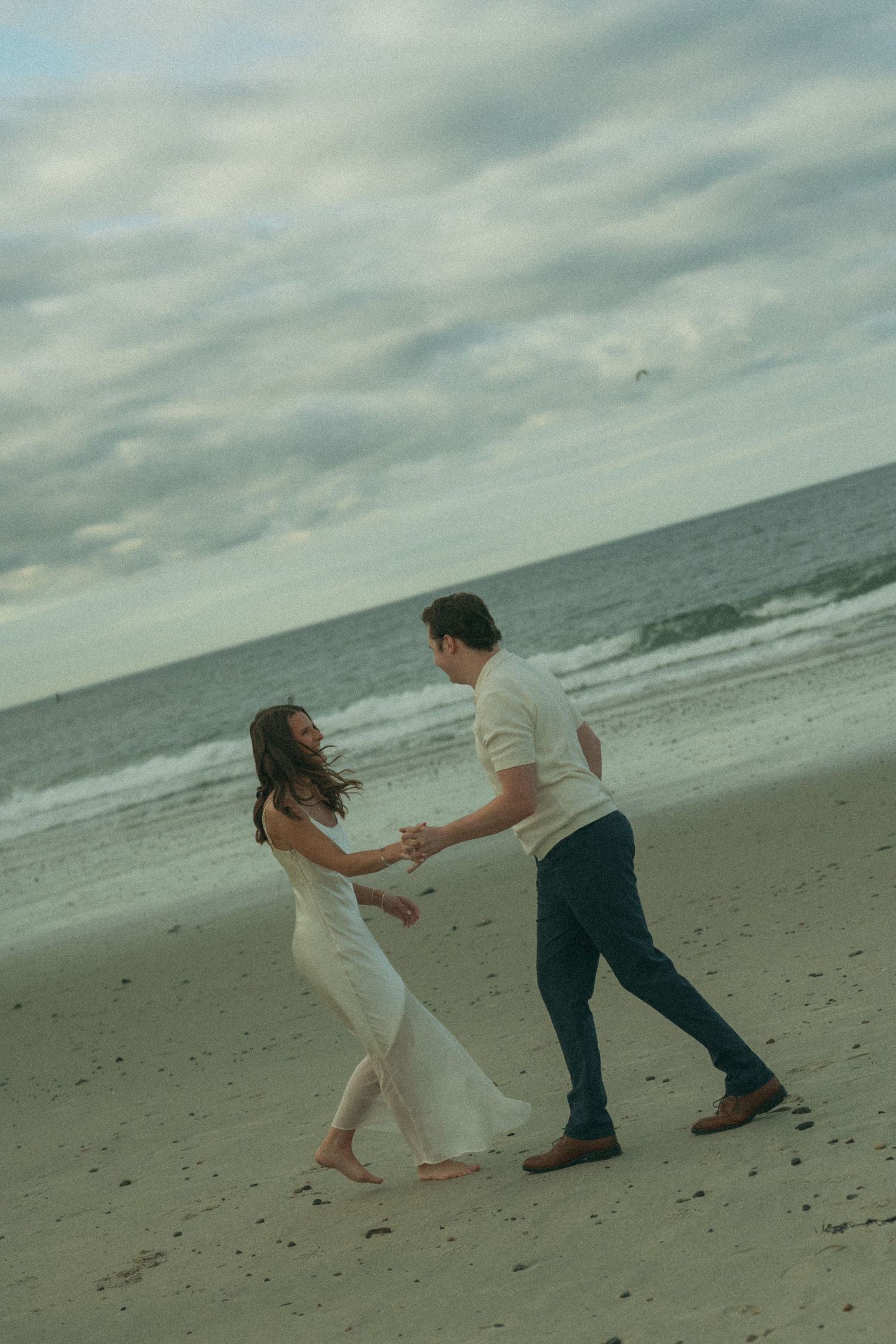 A couple dancing and playing together on a windy beach.