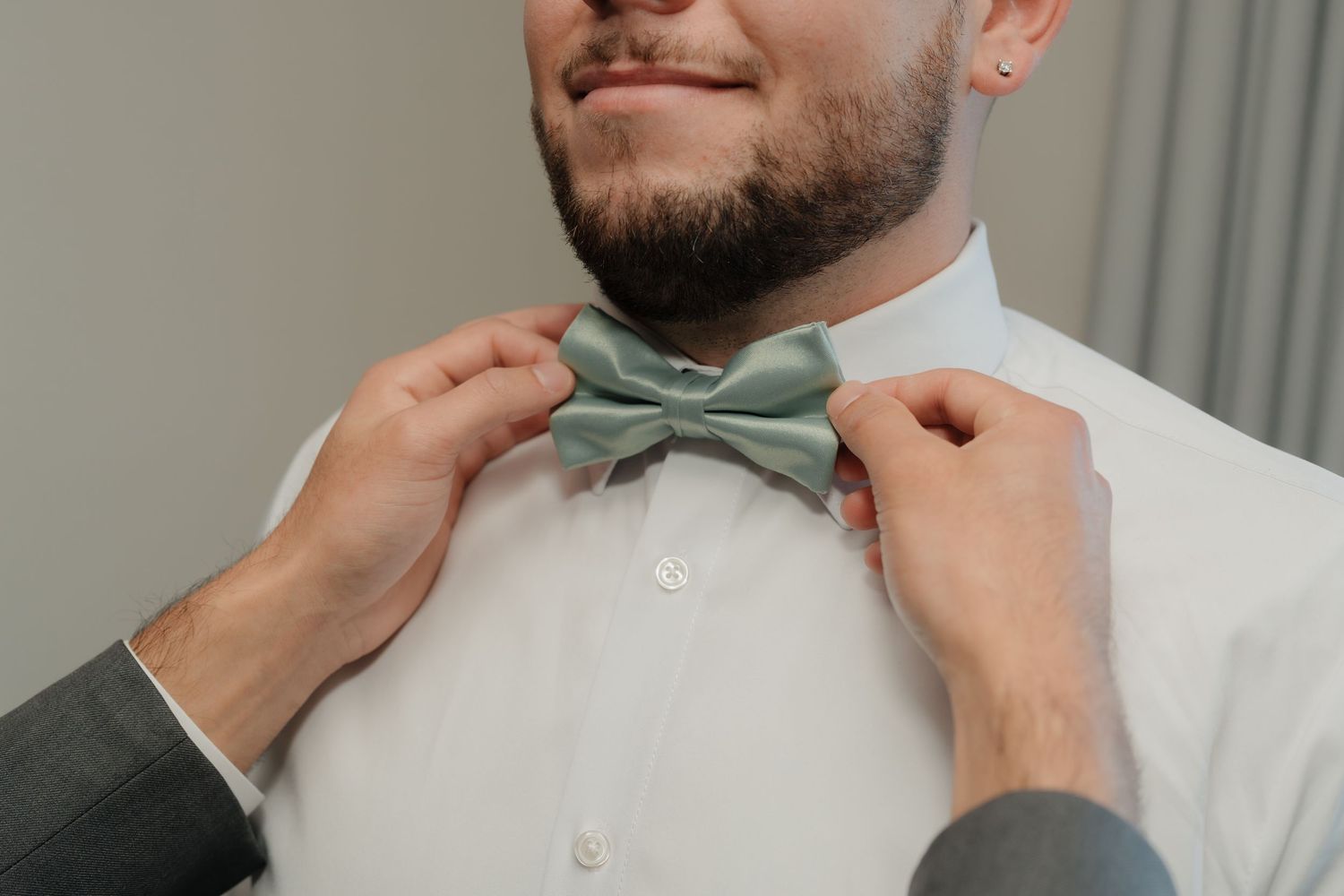 Someone adjusts a mint green bowtie against a white dress shirt.