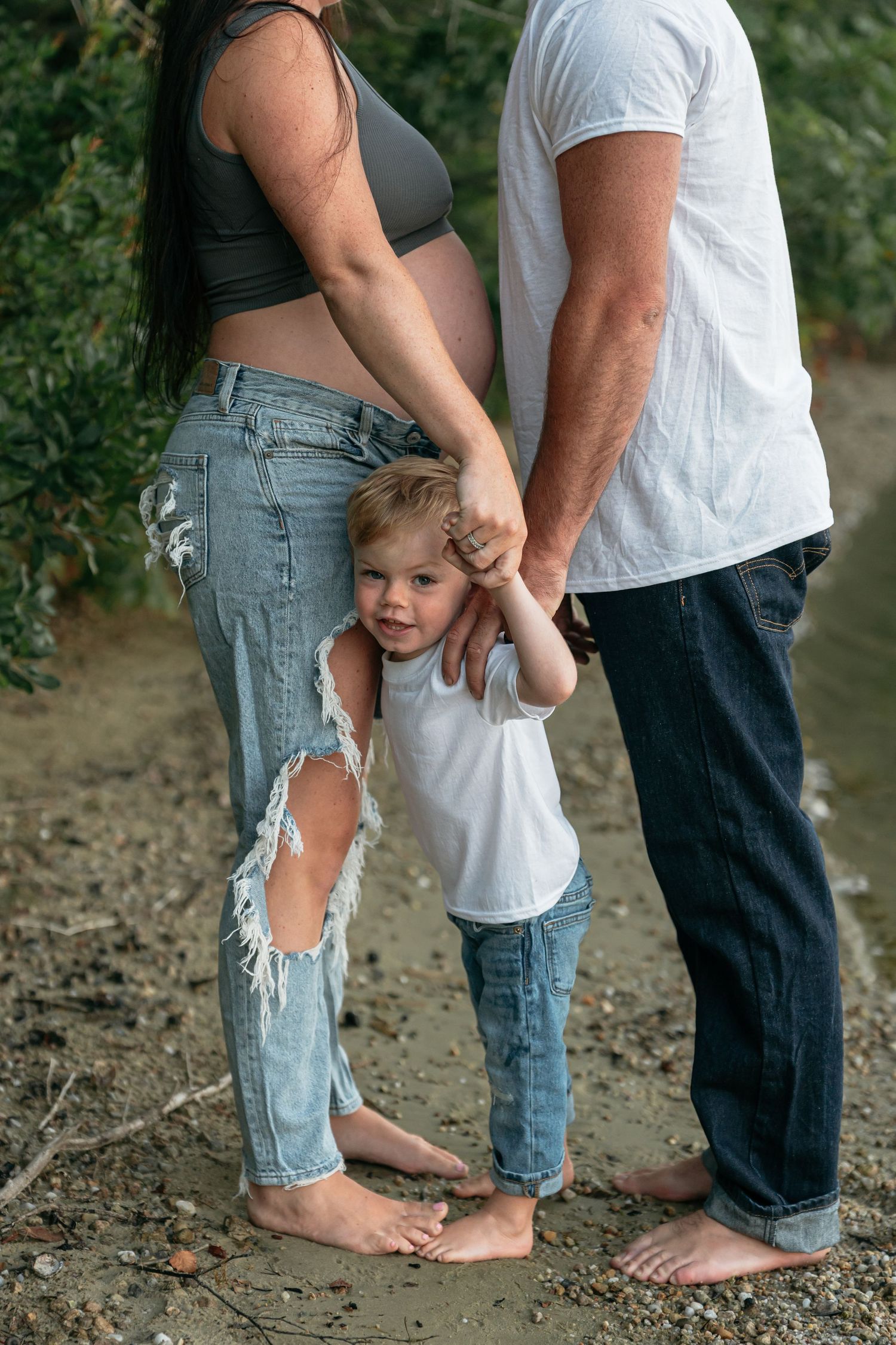 Family members stand barefoot together on a rocky riverbank.