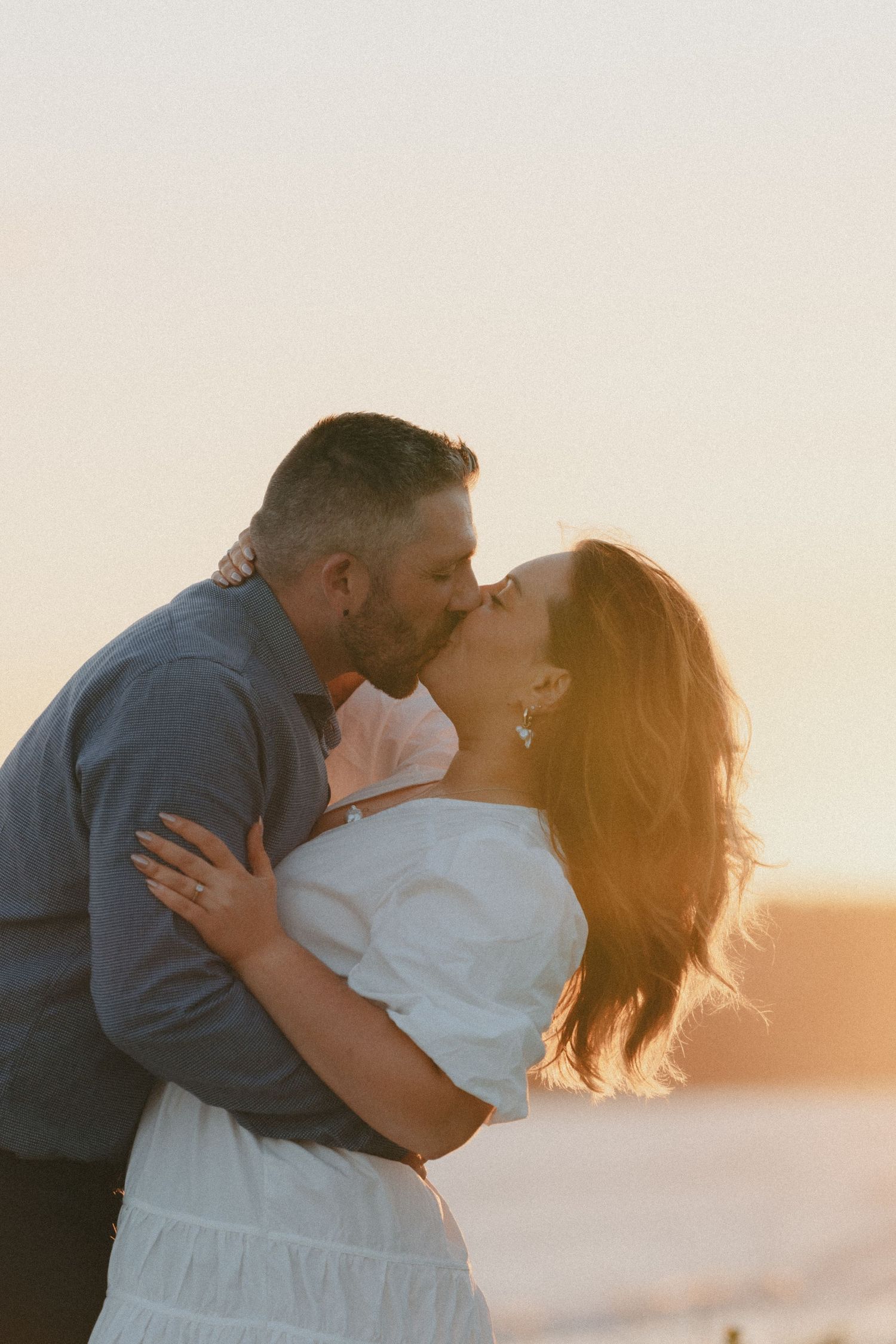 A tender moment shared between a couple during a beach sunset.