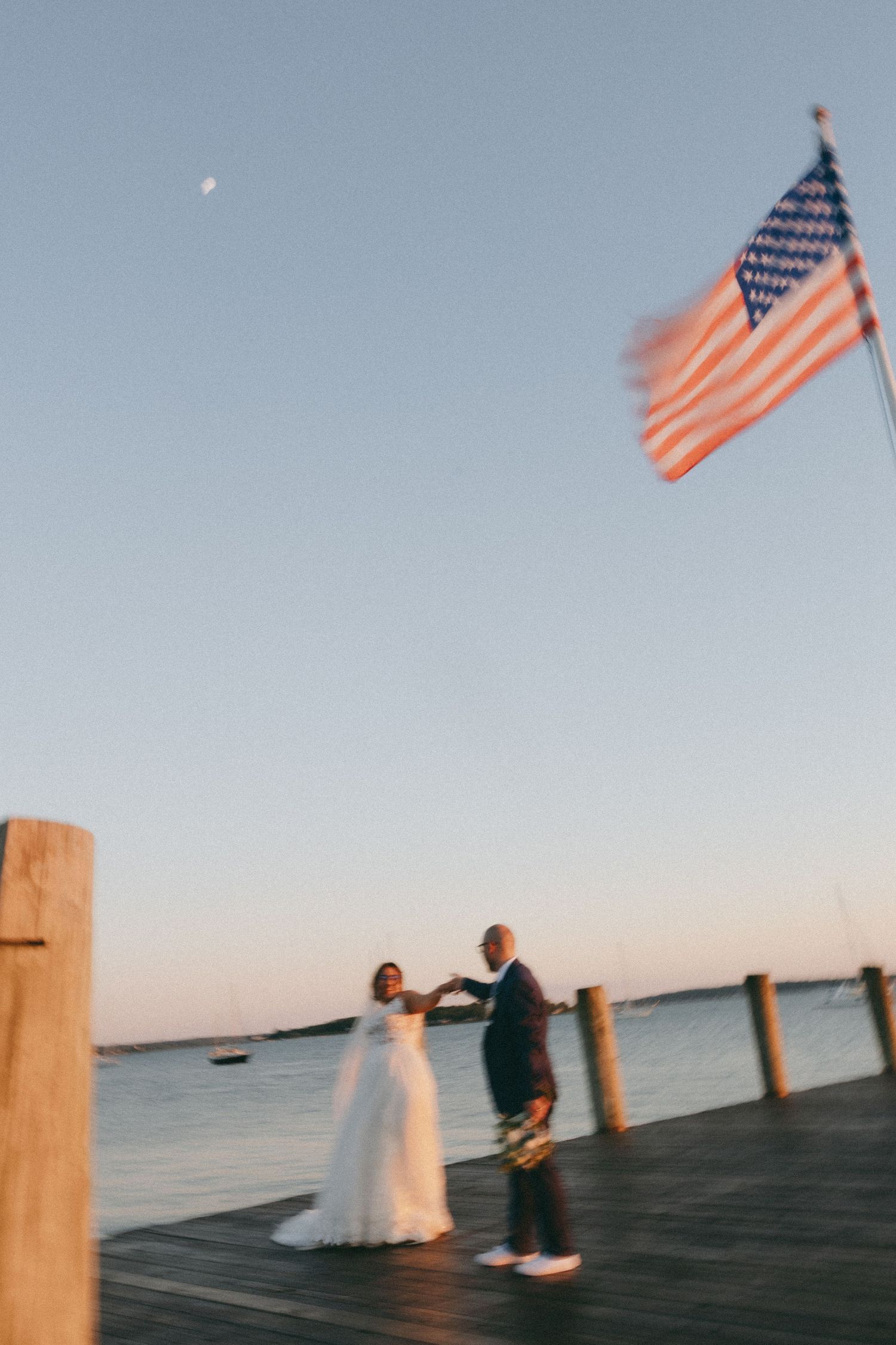 A romantic dock wedding photo with an American flag flying against the evening sky.