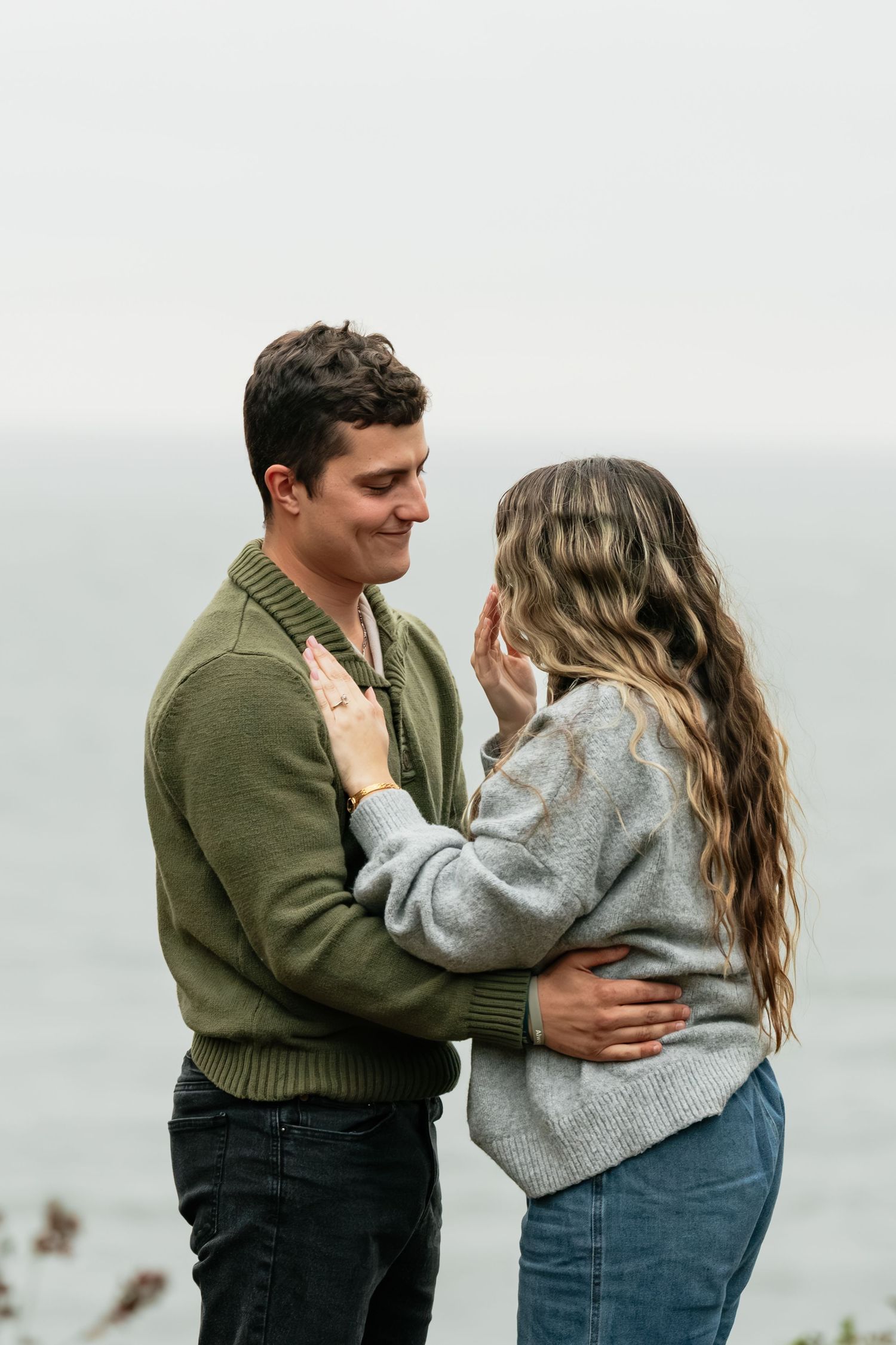 A tender embrace captured against a misty coastal backdrop.
