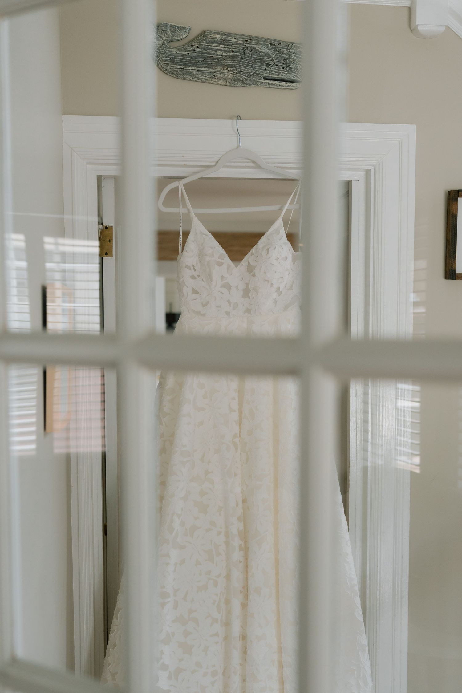 White lace wedding dress hanging in window frame with classic interior molding.