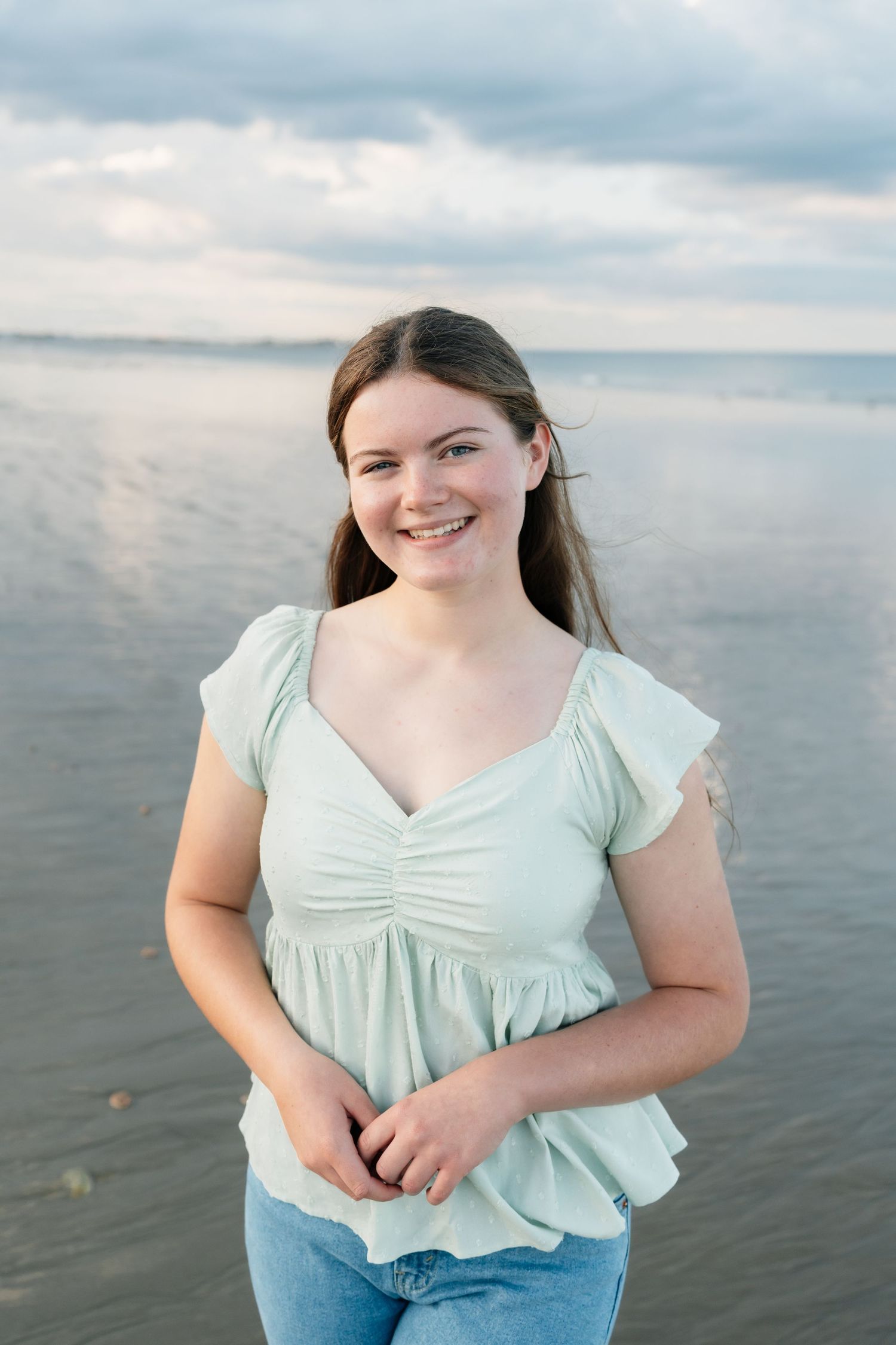 Seaside portrait in mint green blouse and jeans with gentle waves in background.