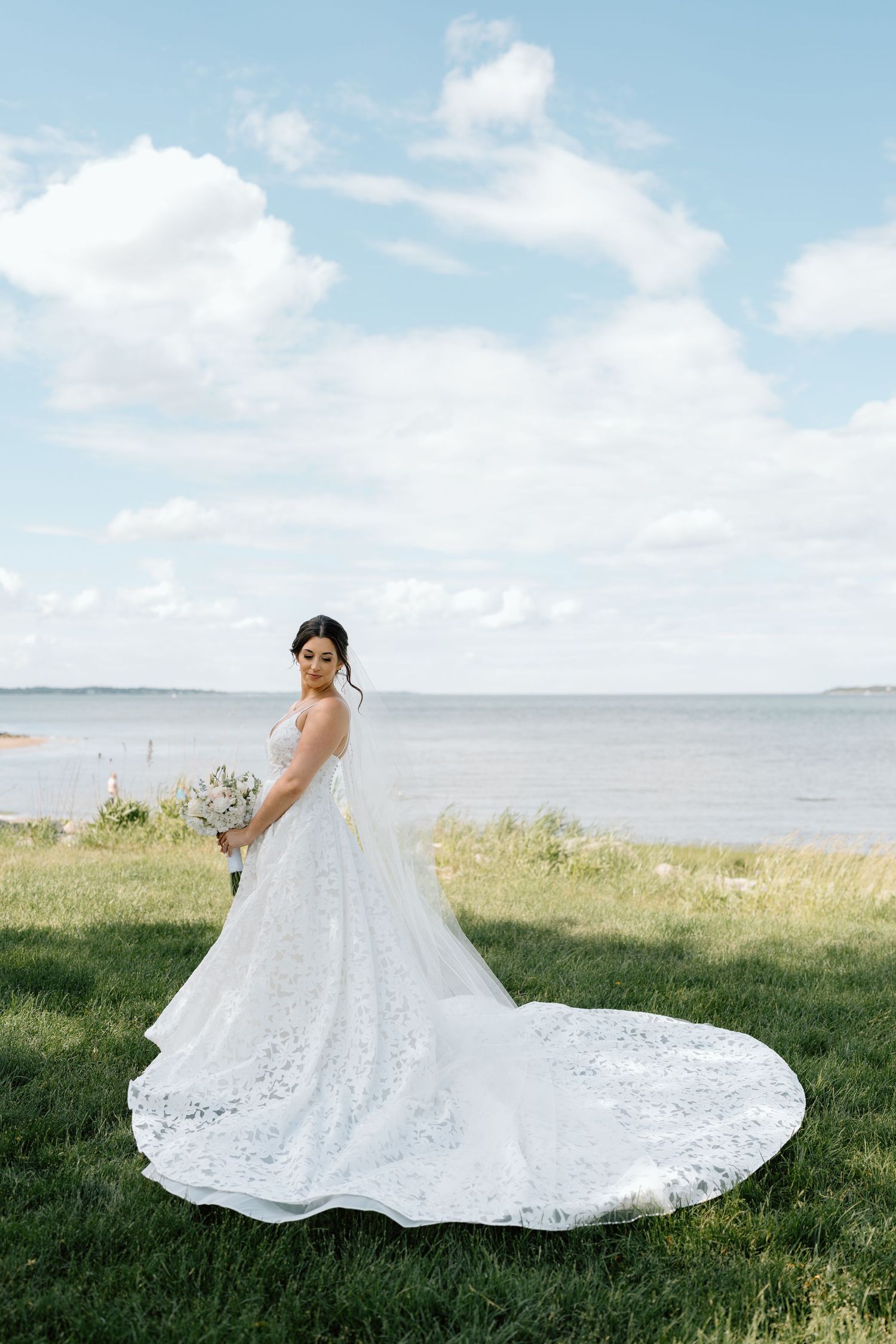 Elegant lace wedding dress with long train photographed against coastal backdrop.