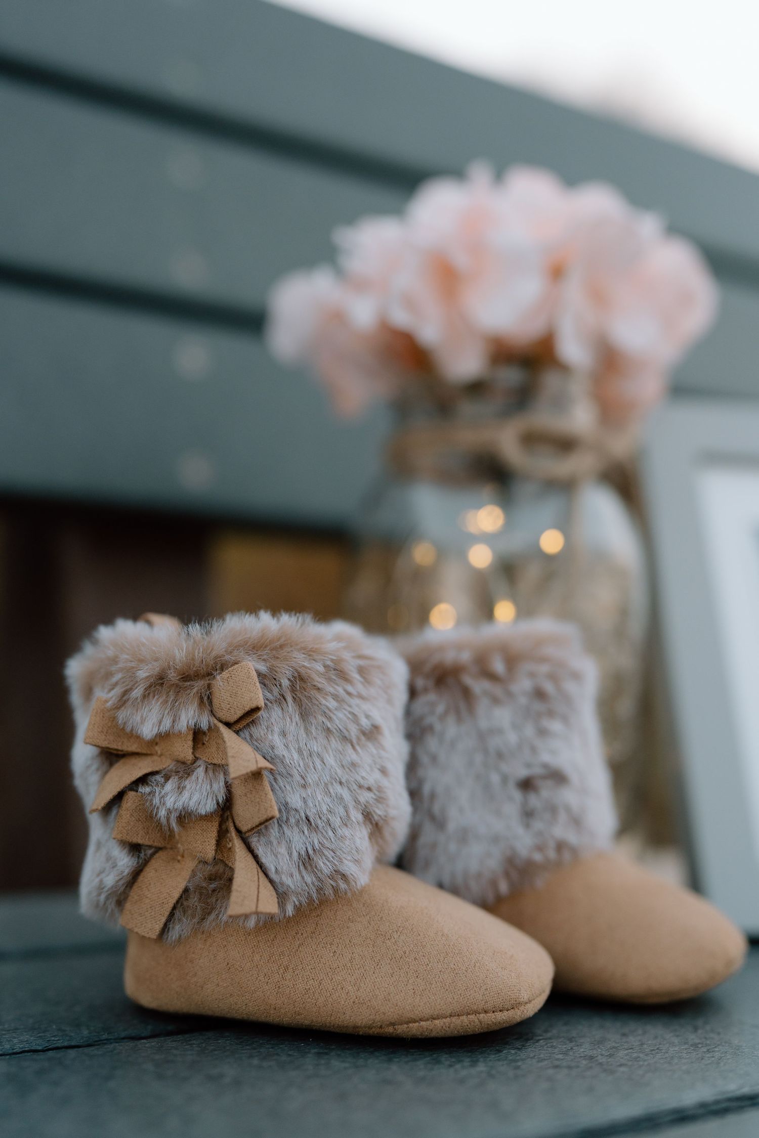 Soft beige baby booties with fur trim and bows photographed with bokeh lights.