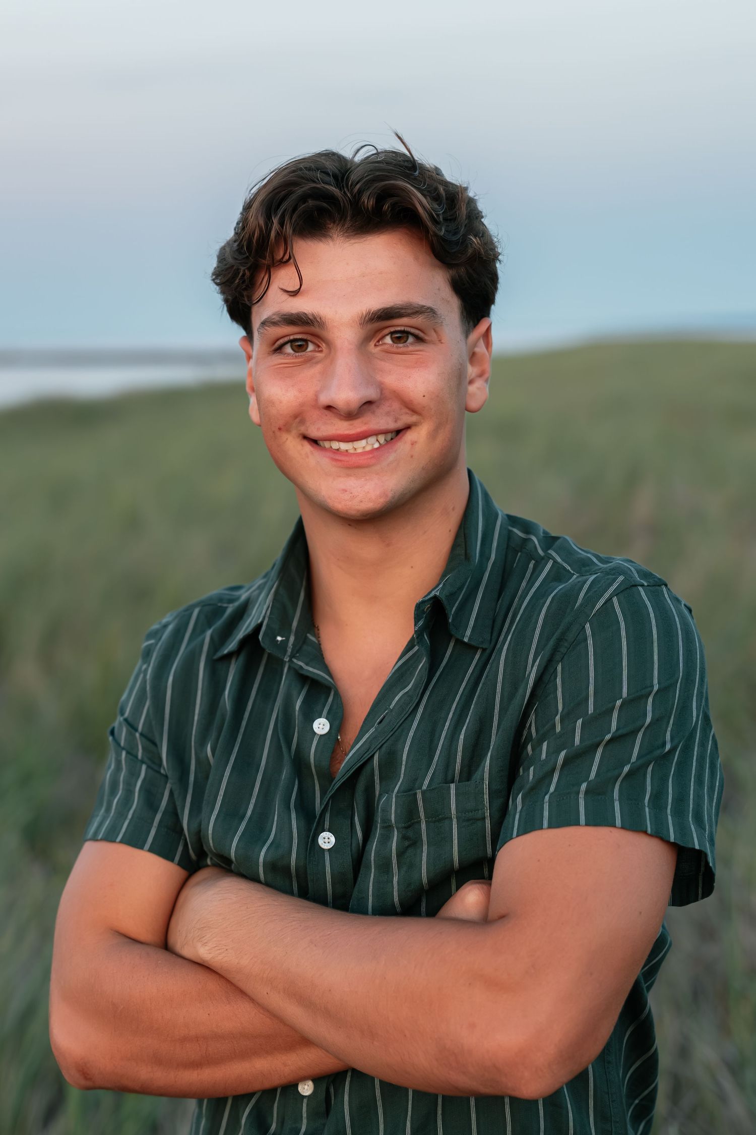 Person in striped green button-down shirt poses outdoors with crossed arms and friendly expression.