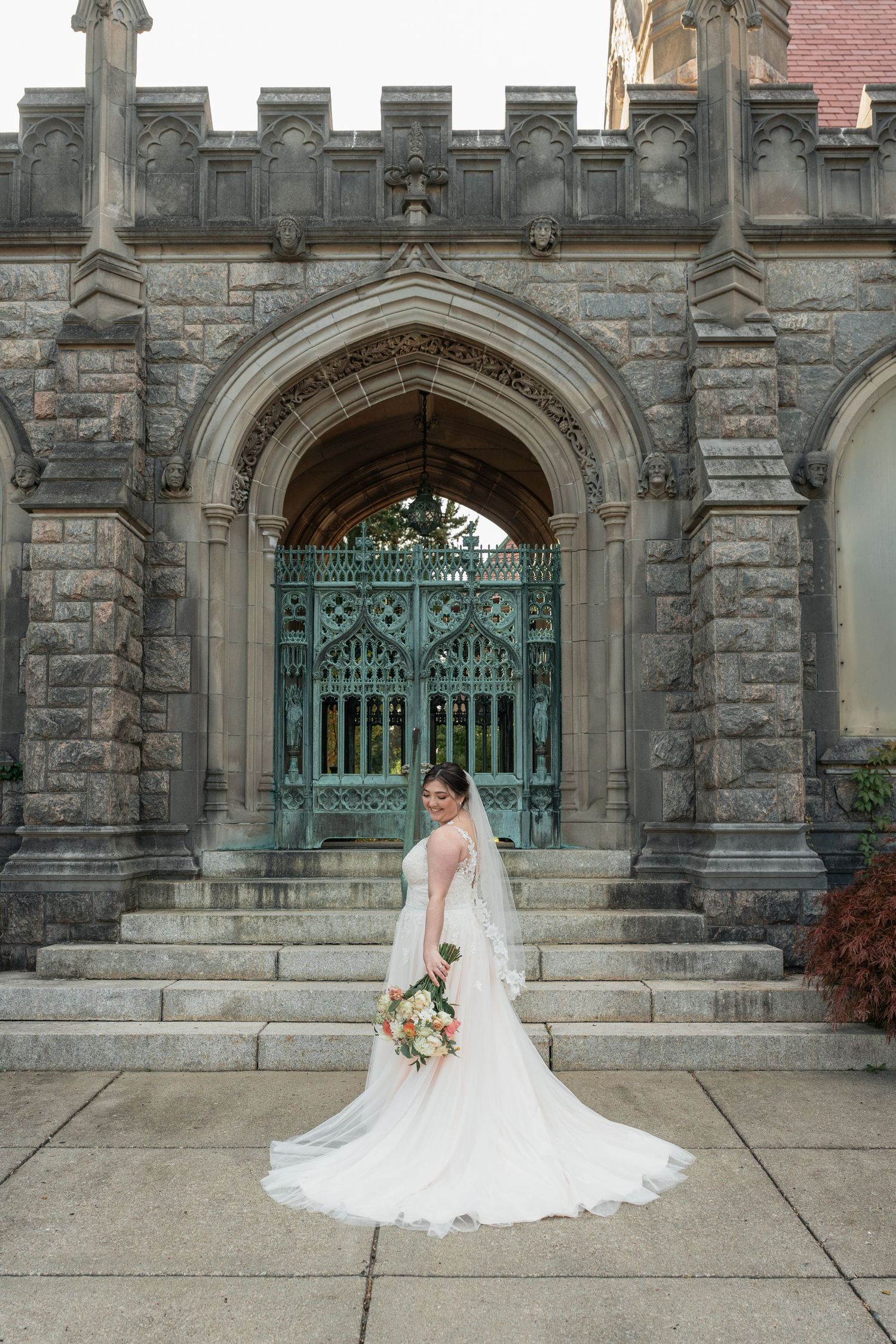 Bride in flowing white dress poses in front of gothic stone architecture.