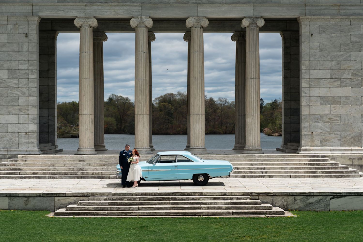 A classic car parked in front of a grand stone colonnade building with steps.