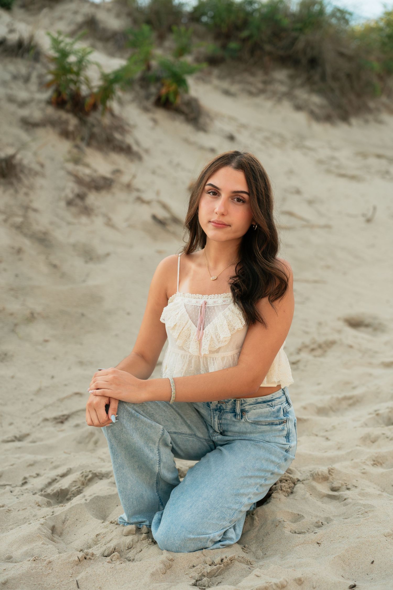 A person in light denim and white top reclines on beach sand during a photo session.