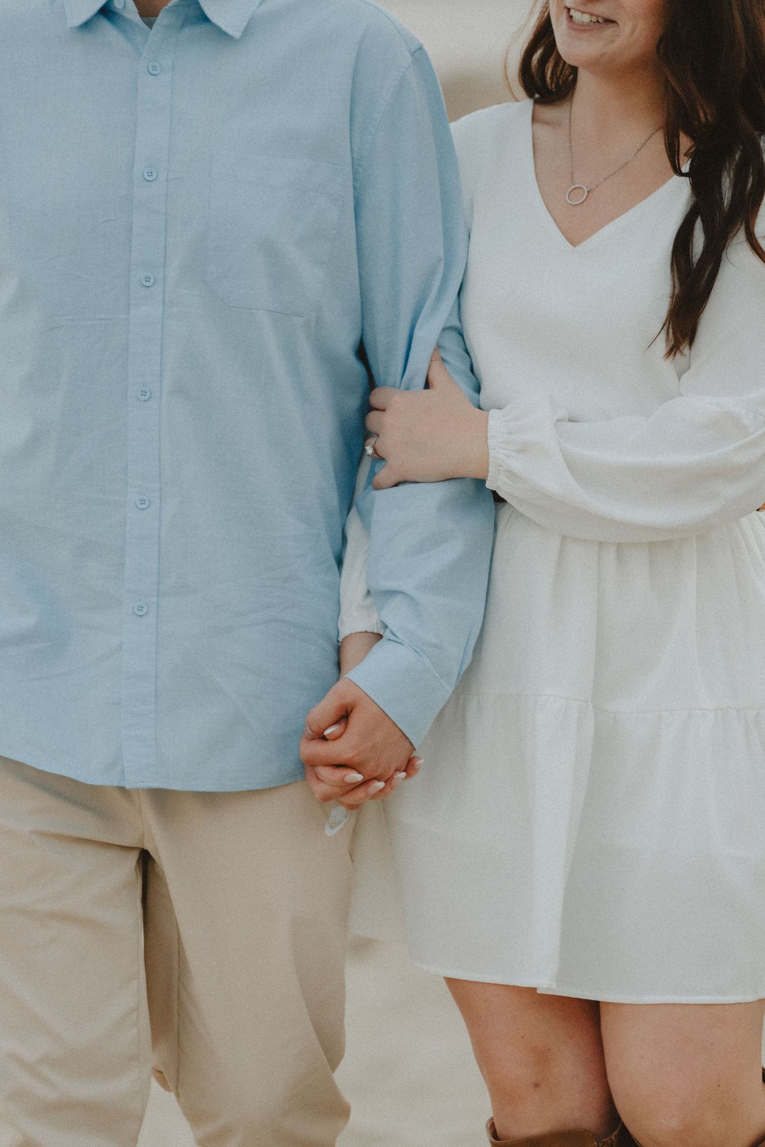 A couple in coordinating blue and white outfits stands together on the beach.