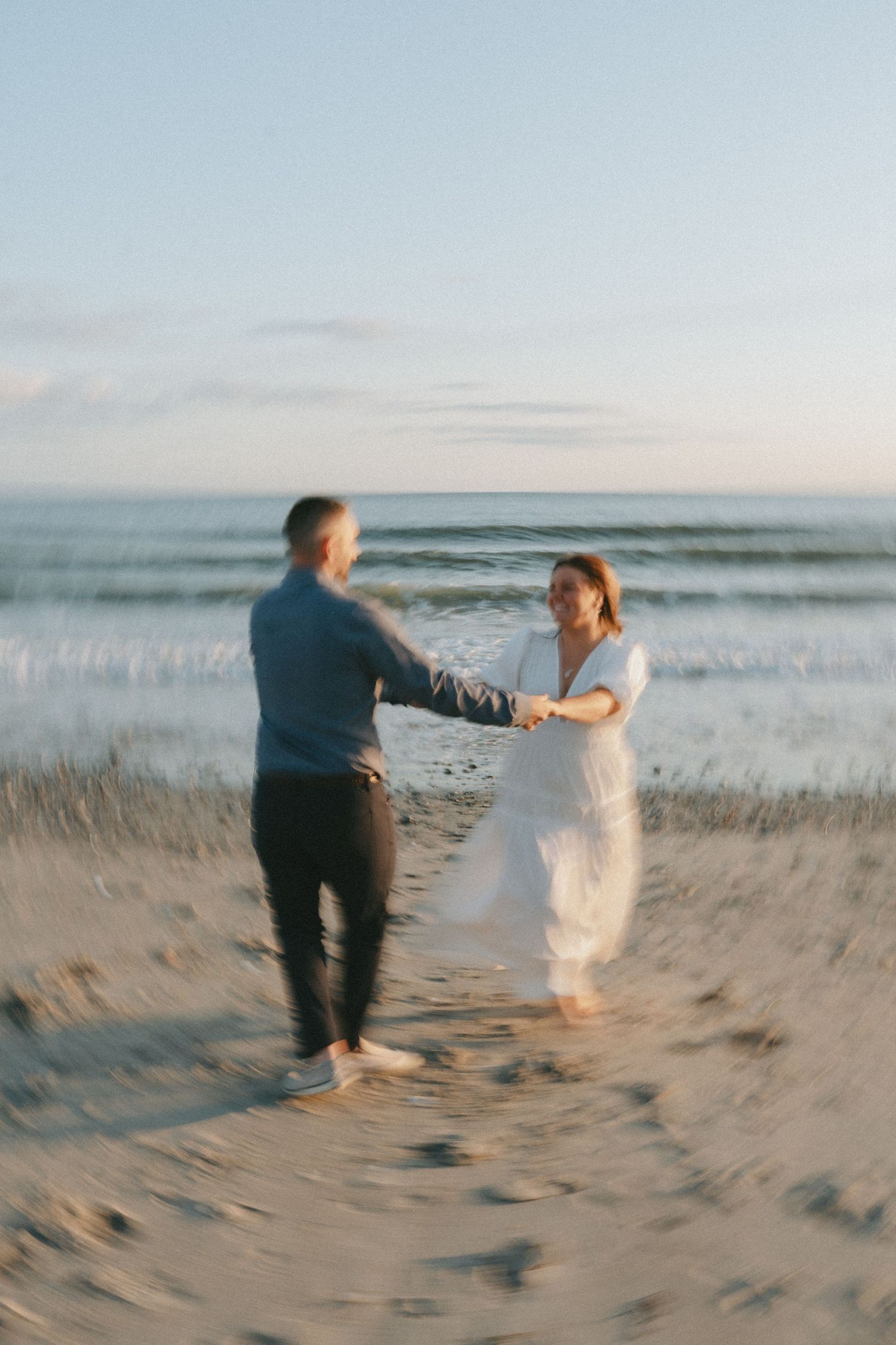 A romantic couple dances together on the beach at dusk.