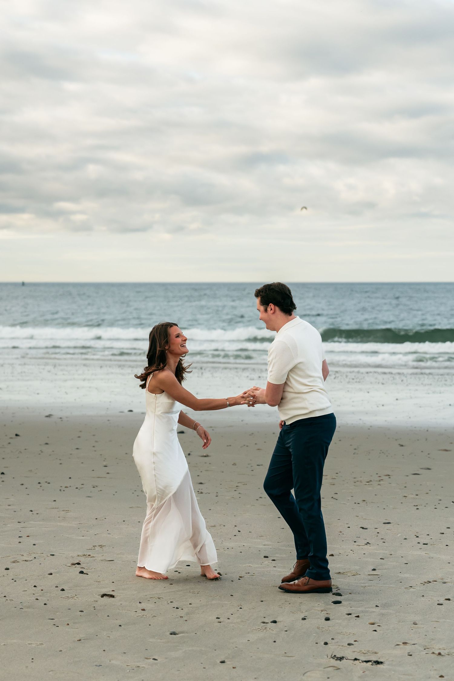 A couple dancing and twirling together on a sandy beach by the ocean.