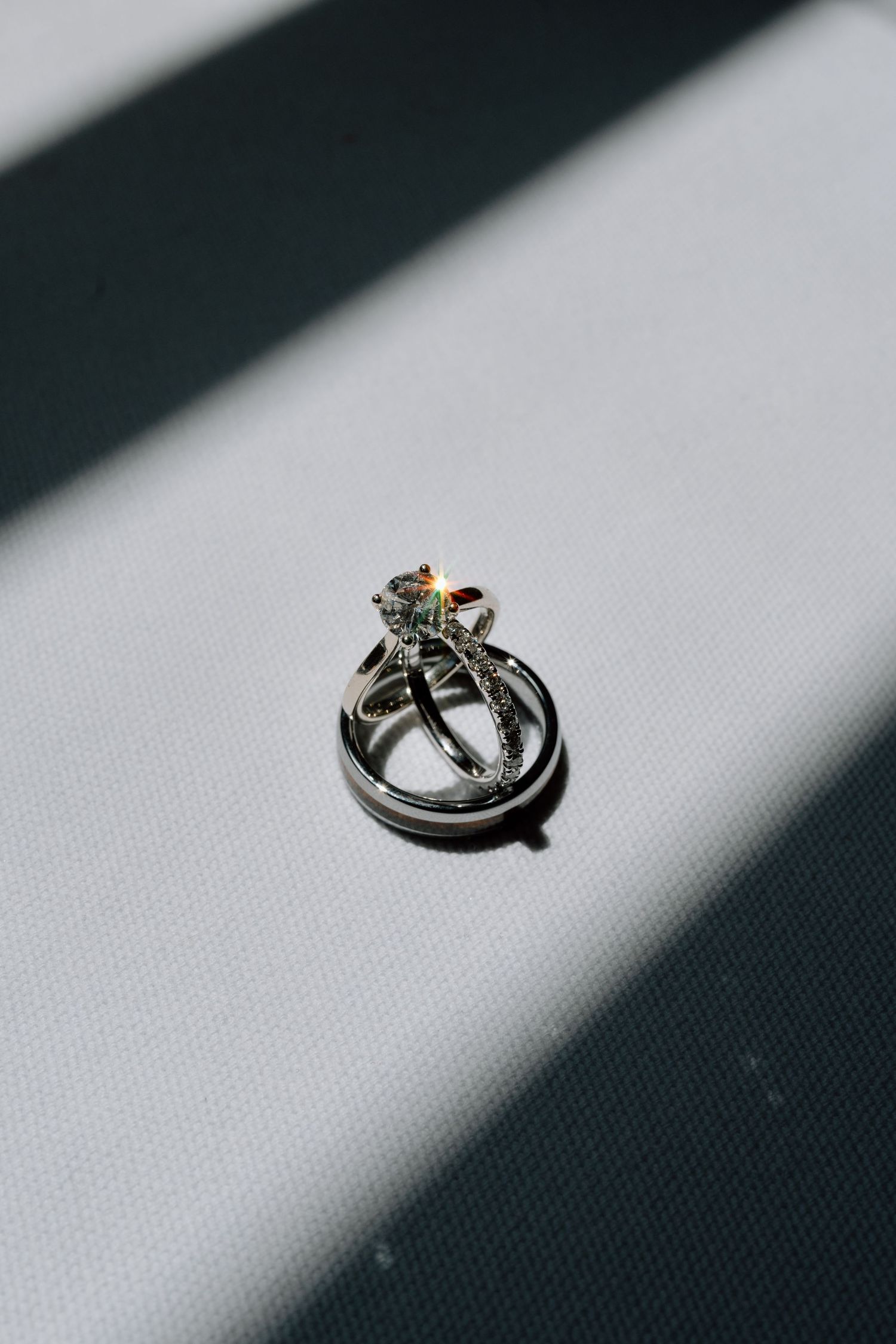 Wedding rings casting dramatic shadows on white fabric in artistic detail shot.
