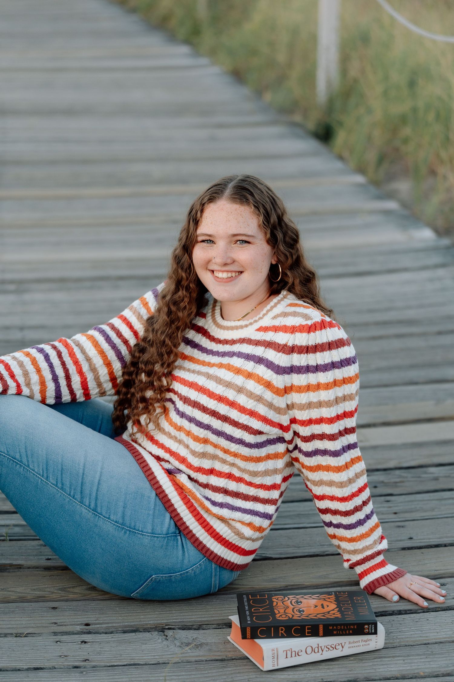 Casual portraits on a wooden boardwalk with books and a striped sweater.