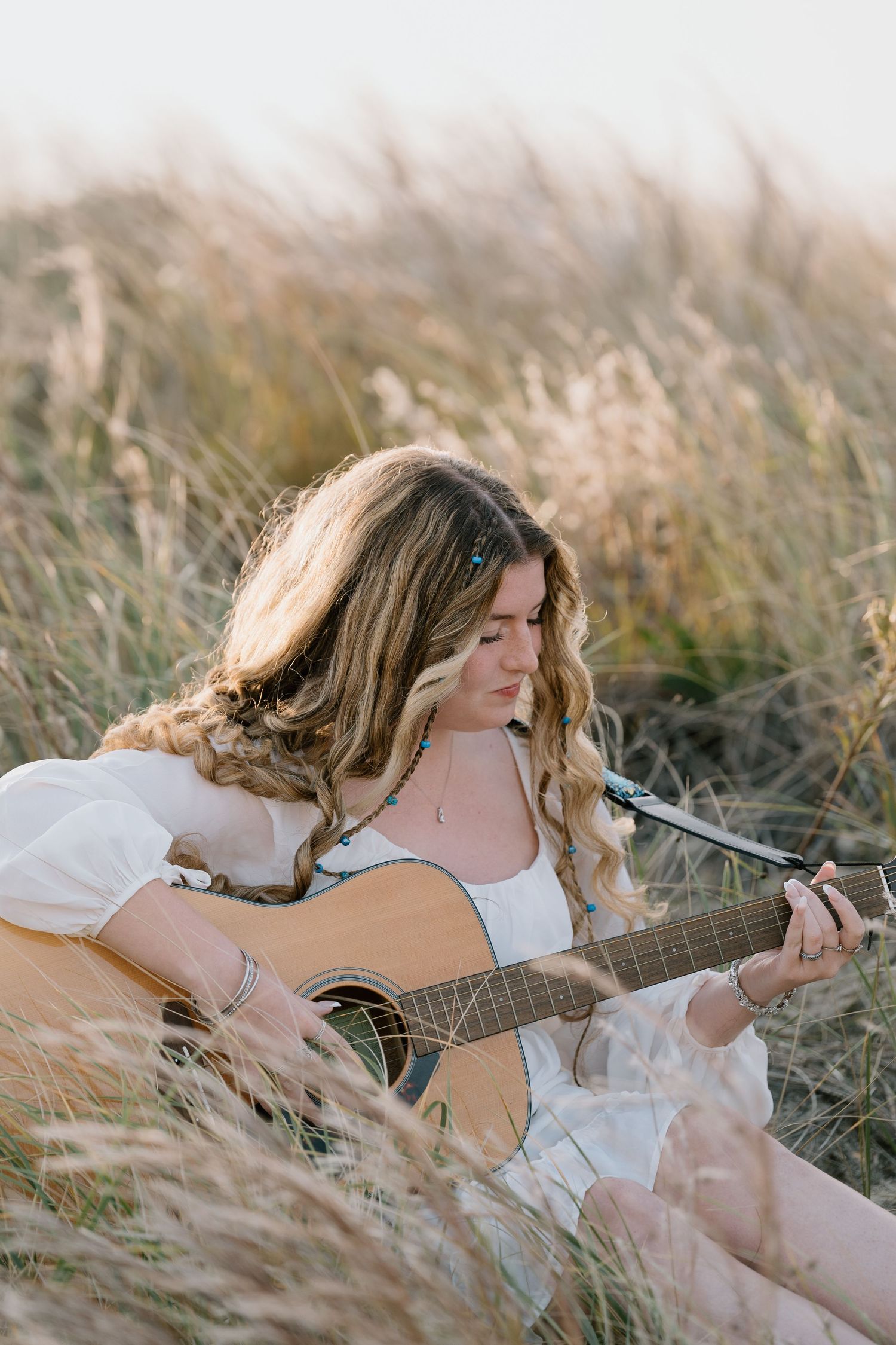 Artistic shot of guitarist in white dress playing among tall grass.