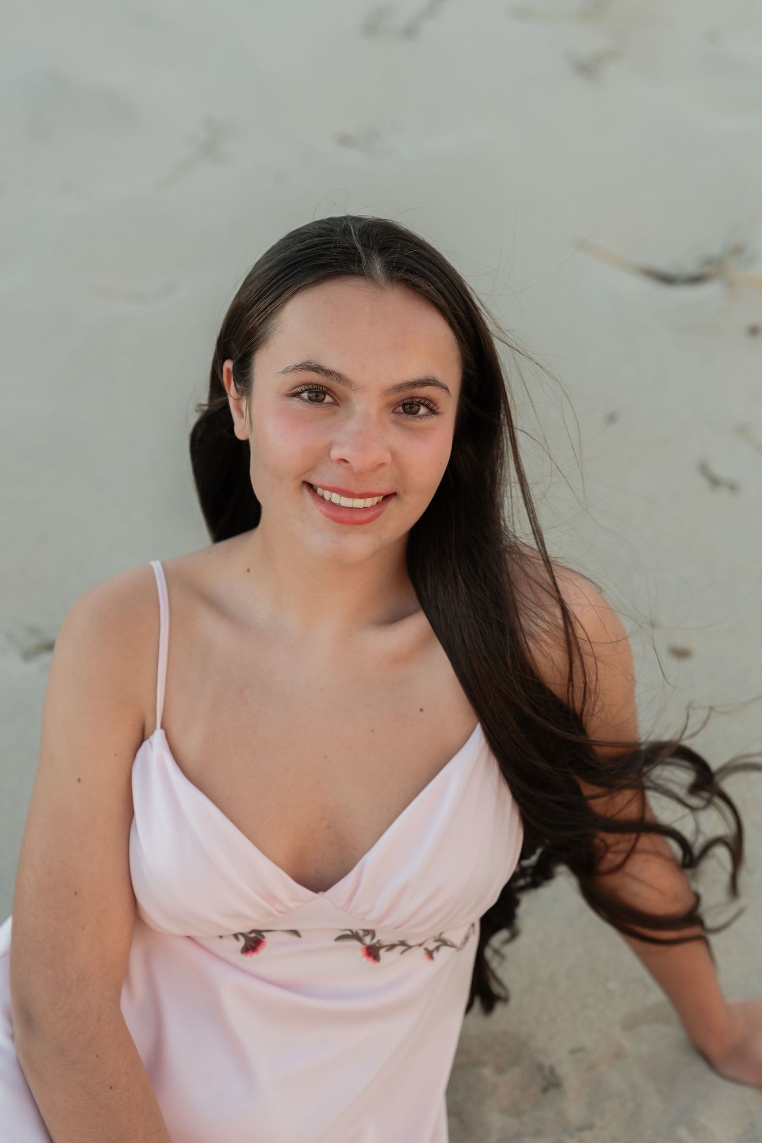 A person in a light pink camisole poses on a sandy beach.