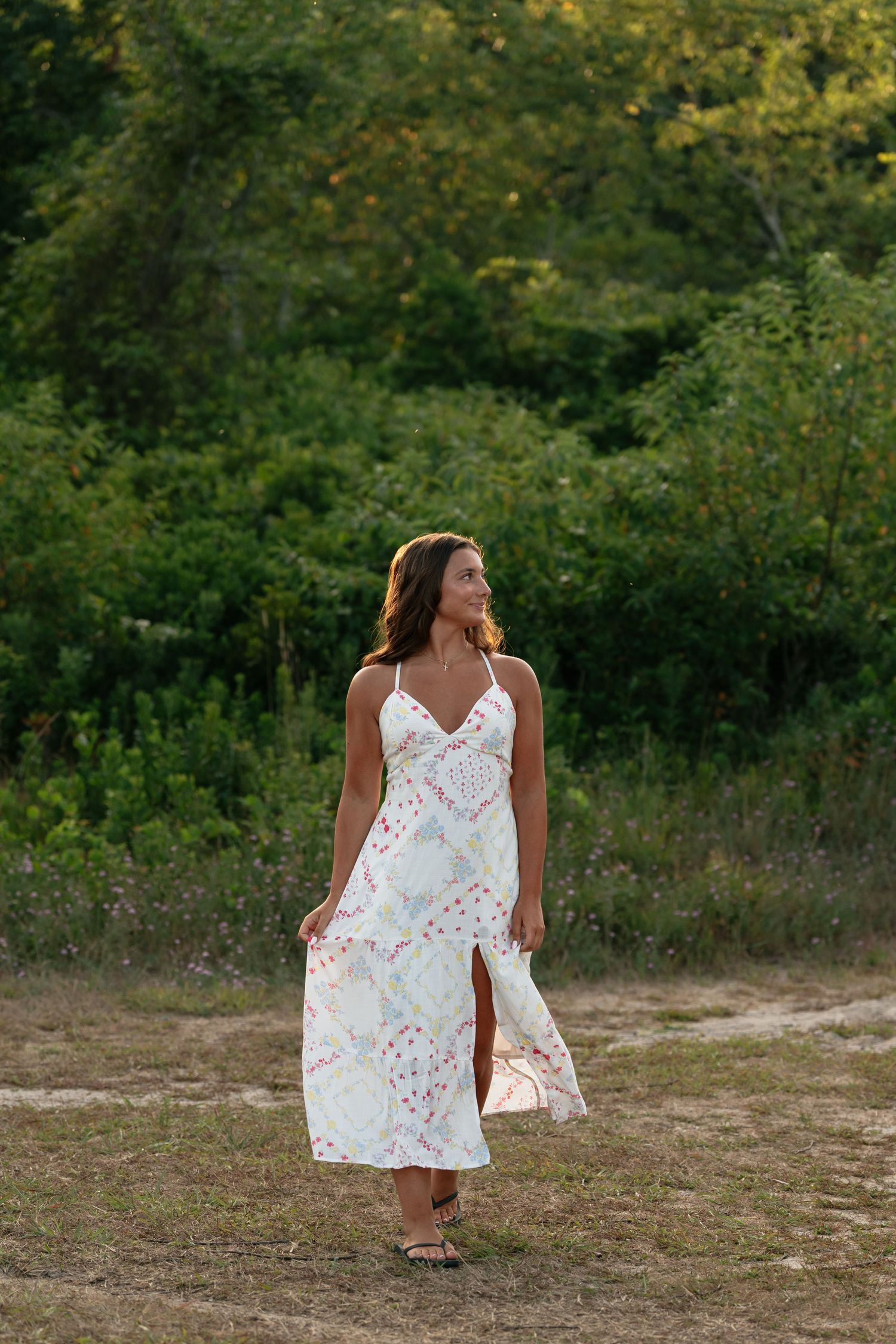 Person in white floral dress walks through natural outdoor setting during photo session.