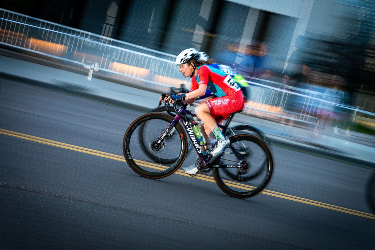 Female cyclist racing at high speed during the Littleton Twilight Criterium in Colorado, captured with motion blur for a dynamic effect.