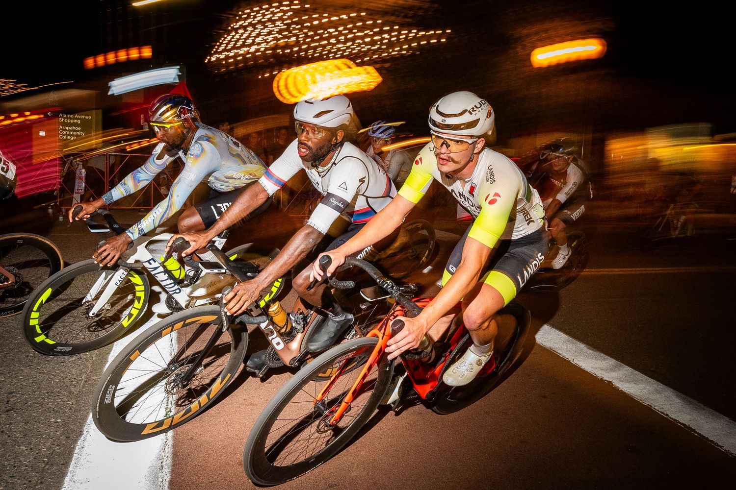 Three male cyclists racing at high speed in the Littleton Twilight Criterium in Colorado, captured with motion blur for a dynamic effect.