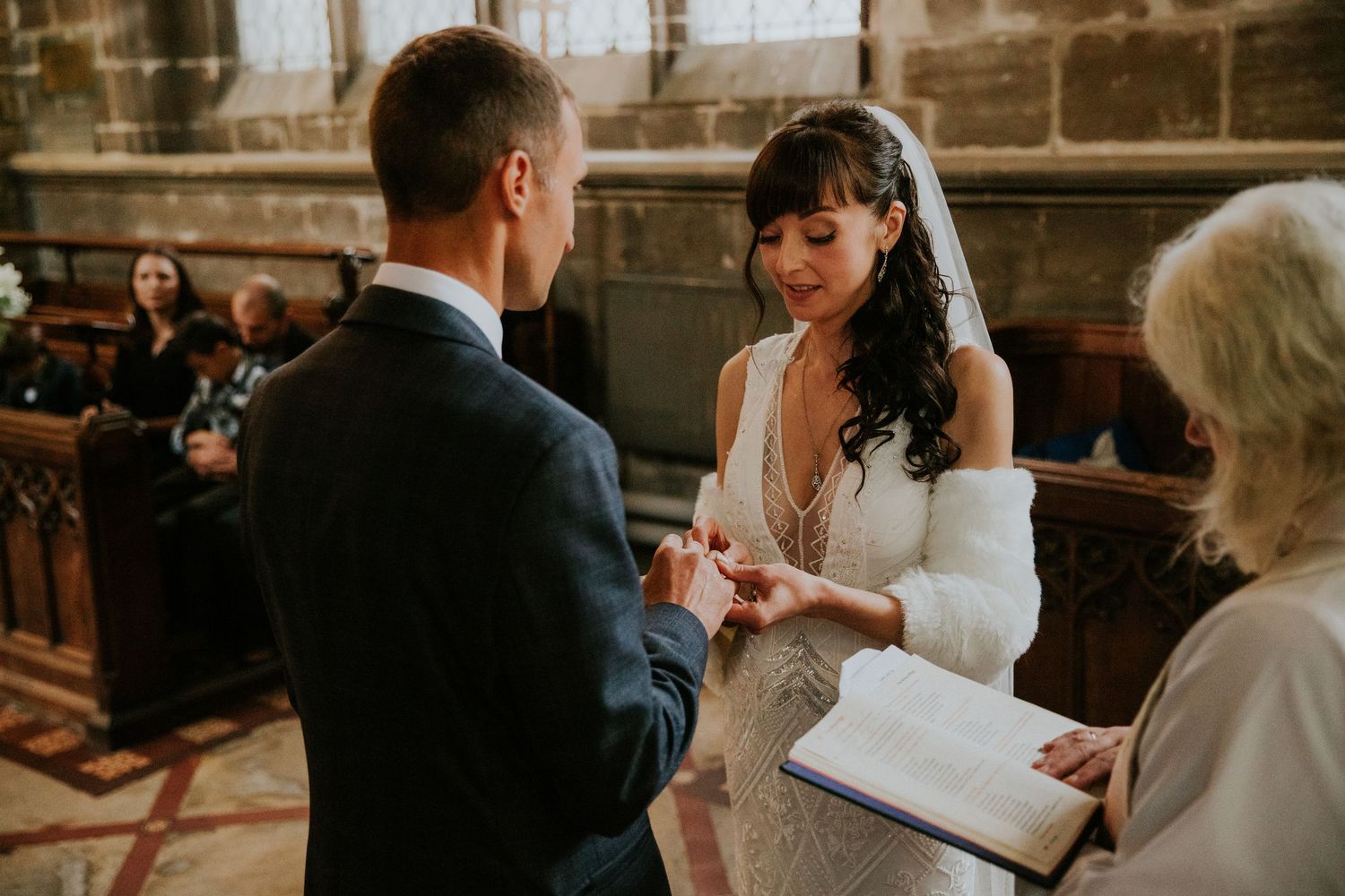 Wedding ceremony participants gather inside historic stone church near stained glass windows.